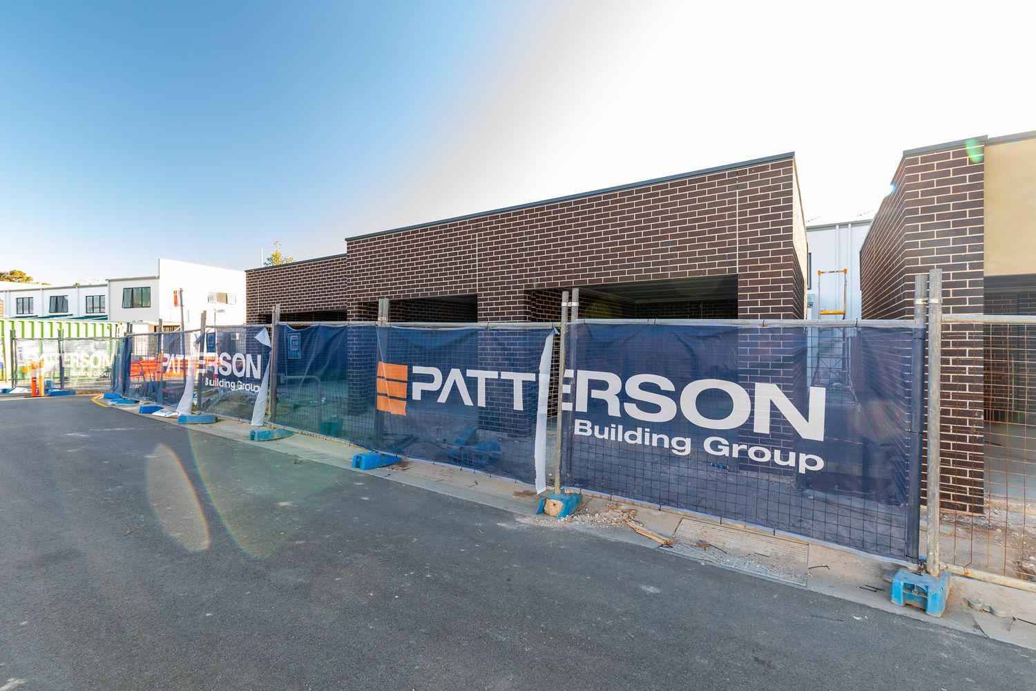 Patterson Building Group banner on temporary fencing in front of new brick townhouses under construction on a quiet street.