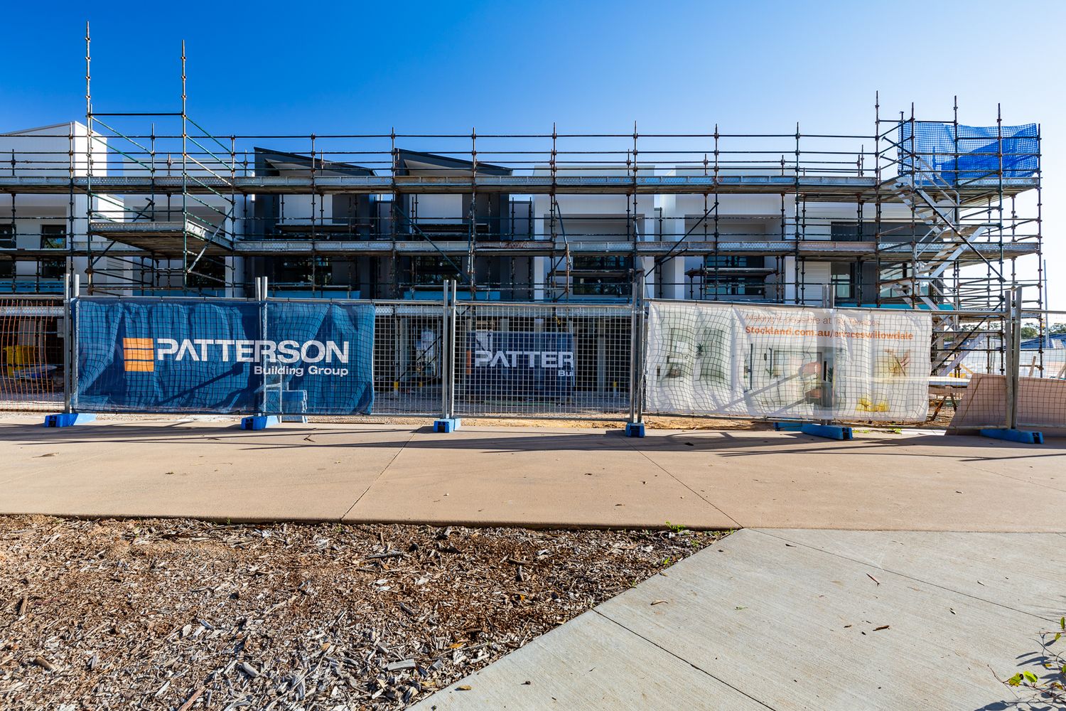 Townhouse building site wrapped in scaffolding behind a fence with Patterson Building Group banners and a gravel footpath.