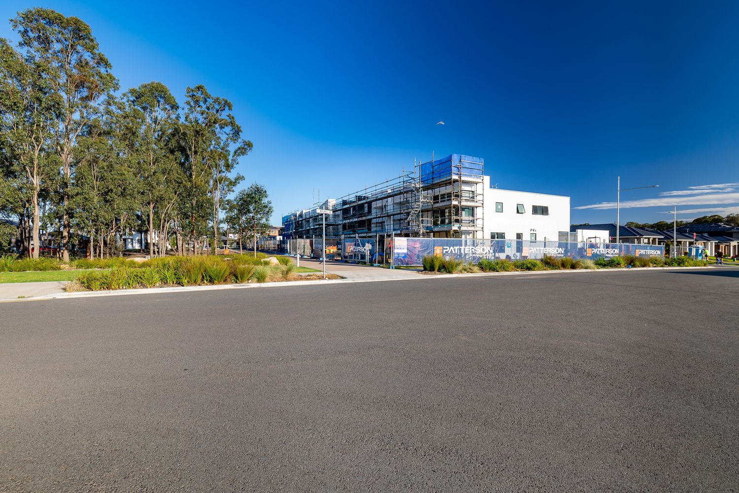 Multi-storey building under construction with scaffolding beside a quiet car park and eucalyptus trees on a sunny day.