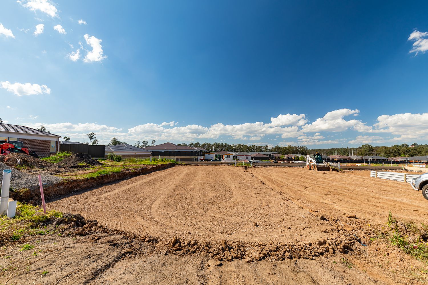 Cleared and levelled vacant building lot with bare dirt under a bright blue sky, ready for new home construction in a suburb.
