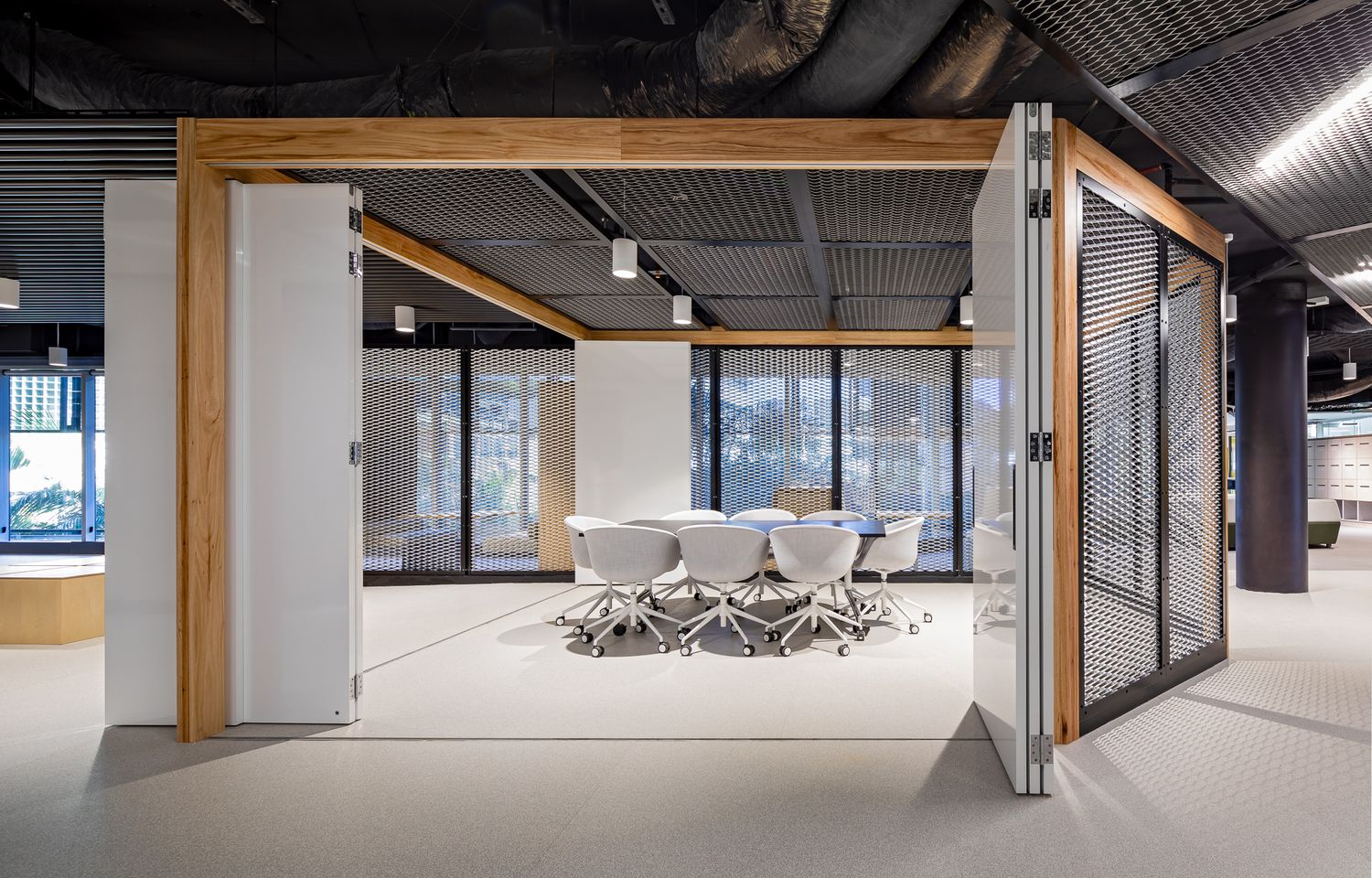 Modern meeting room with white chairs and a round table, enclosed by timber-framed sliding doors under an exposed black industrial ceiling.