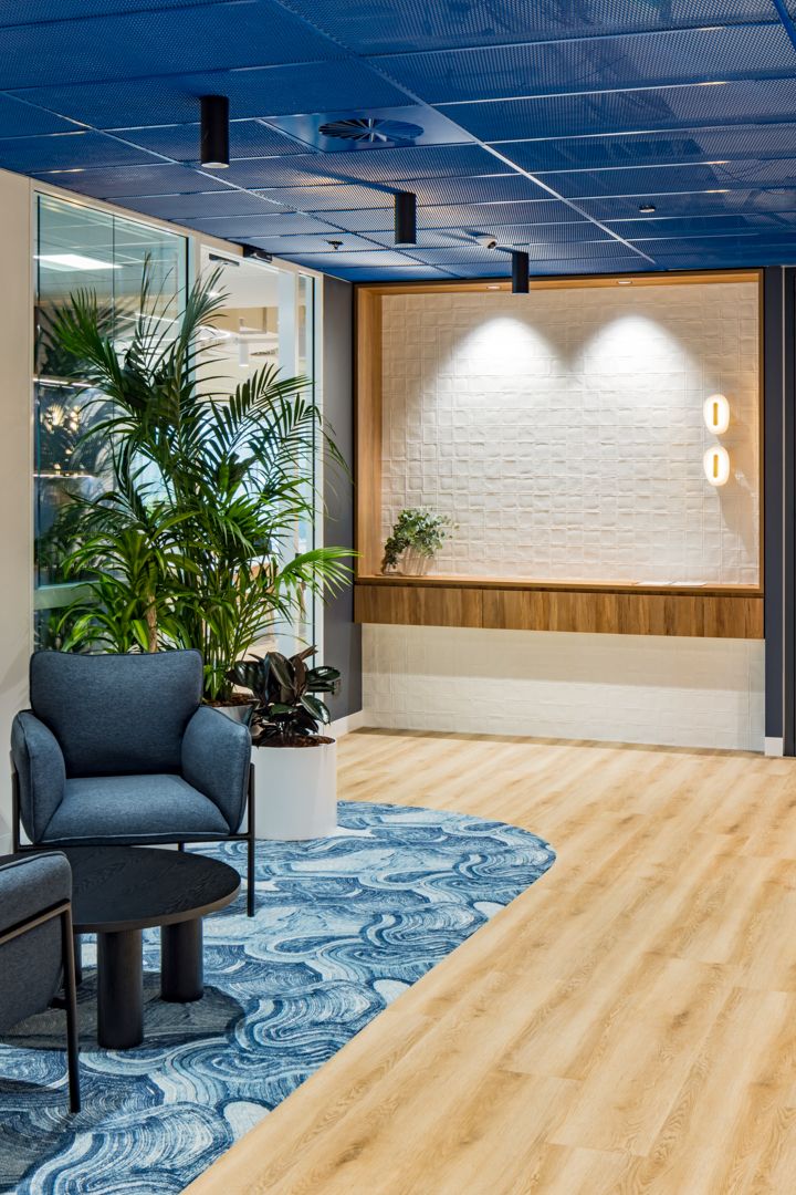 Contemporary office lounge with navy armchairs, potted palms, a blue wave-patterned rug and a white brick feature wall.
