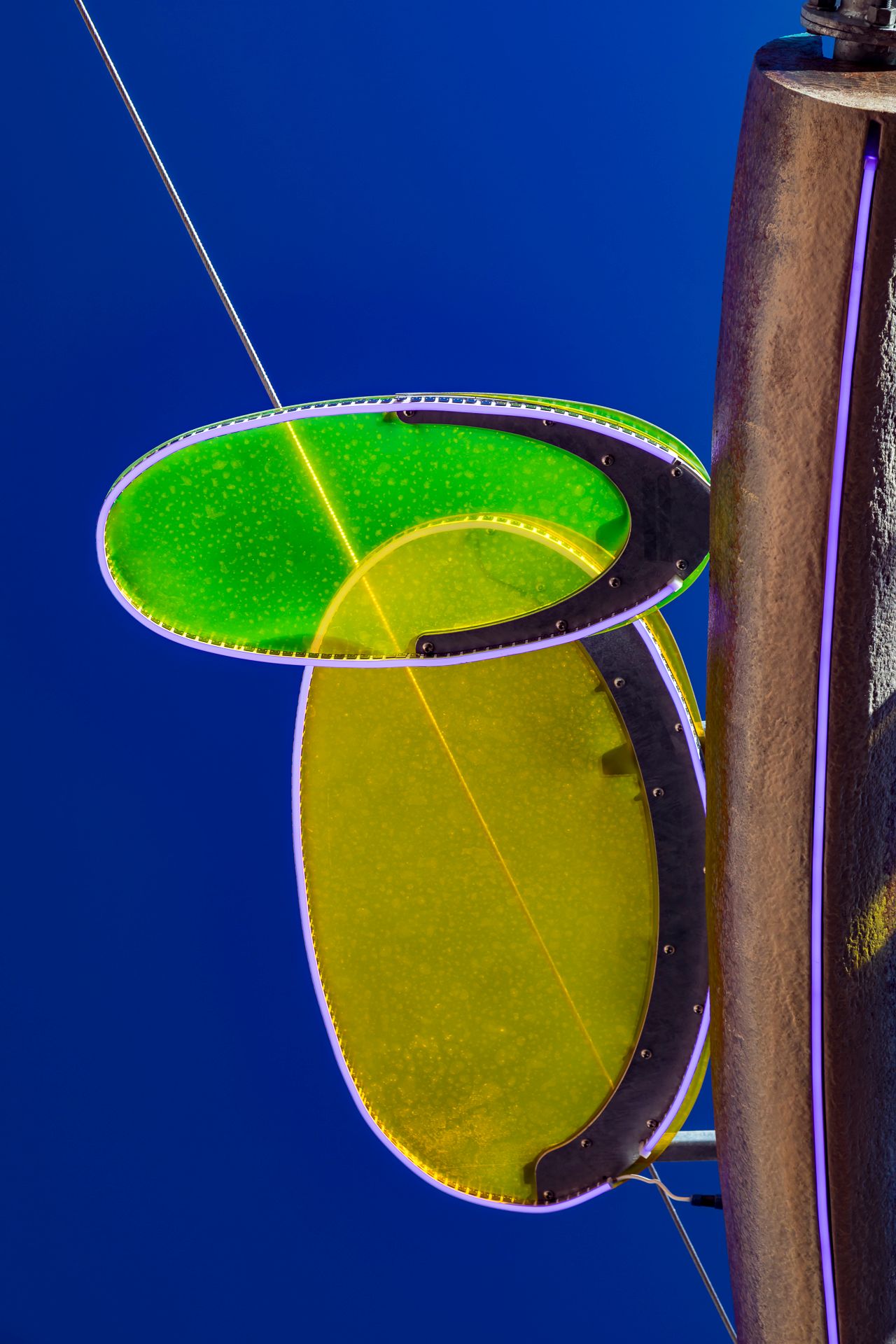 Close-up of two glowing green and yellow oval discs with illuminated edges against a deep blue sky beside a bronze sculpture.