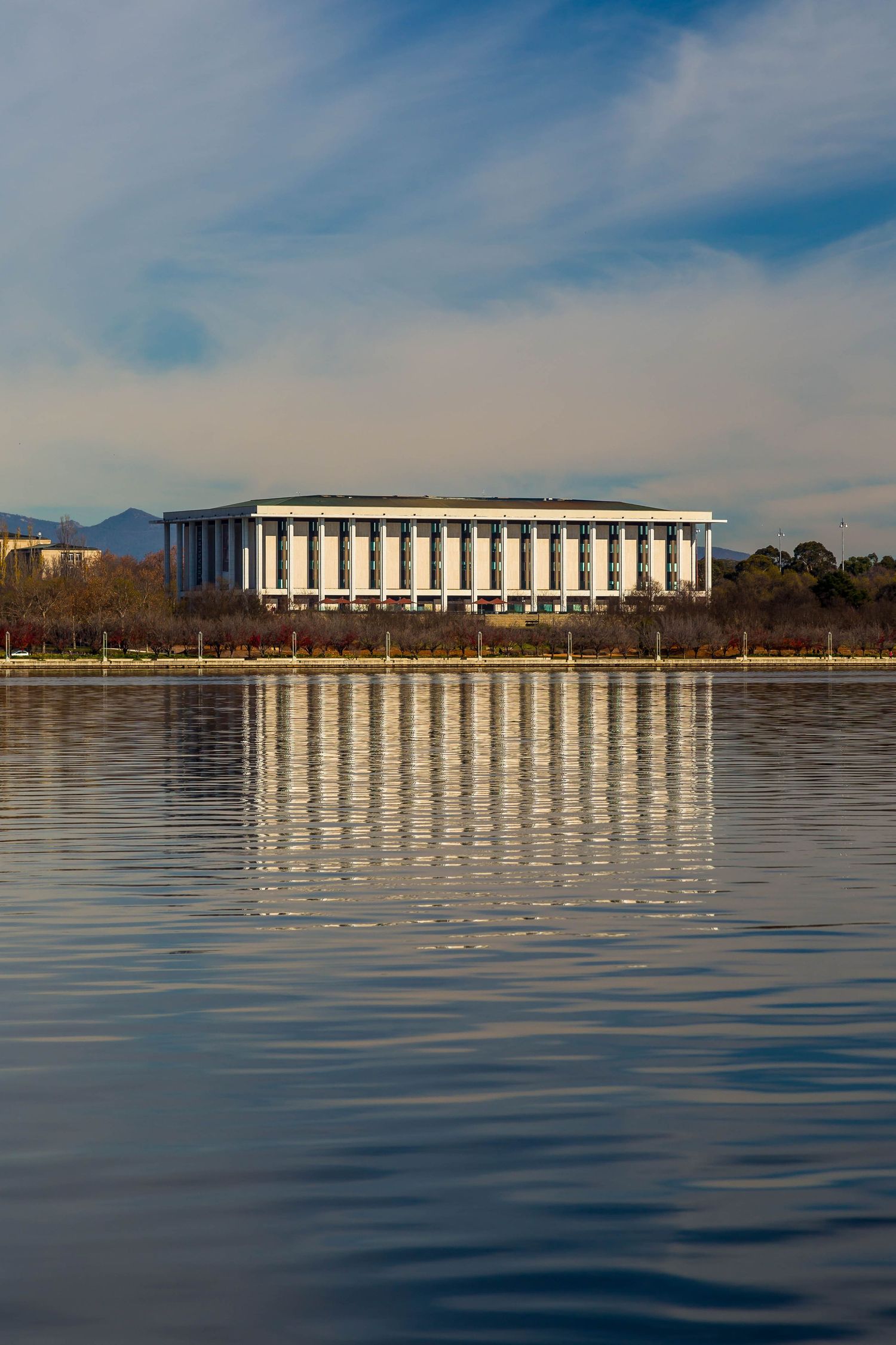 Neoclassical-style National Library of Australia with white columns reflected in the calm waters of Lake Burley Griffin.