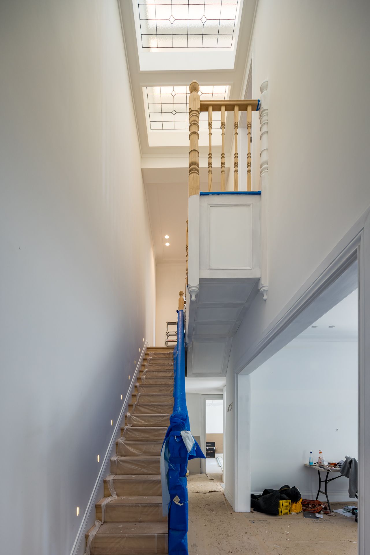 Long hallway with a covered staircase, timber balustrade and skylights in a home under renovation.