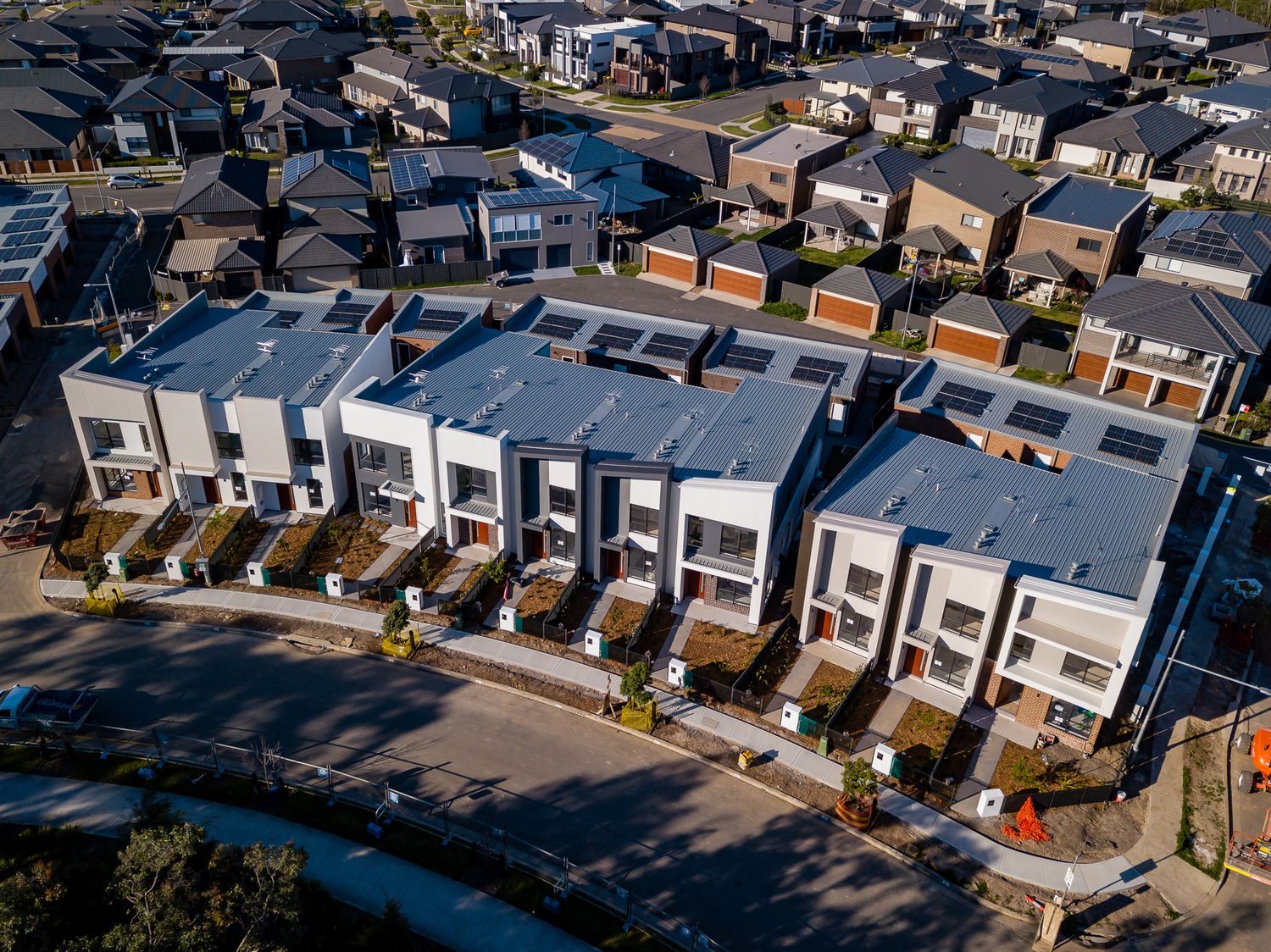 Aerial view of modern white and grey townhouses beside a curved street in a newly developed suburban neighbourhood.