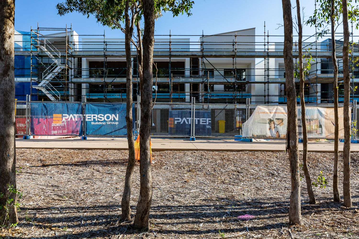 Townhouse development under construction behind trees, with scaffolding, site hoarding and Patterson building signage.