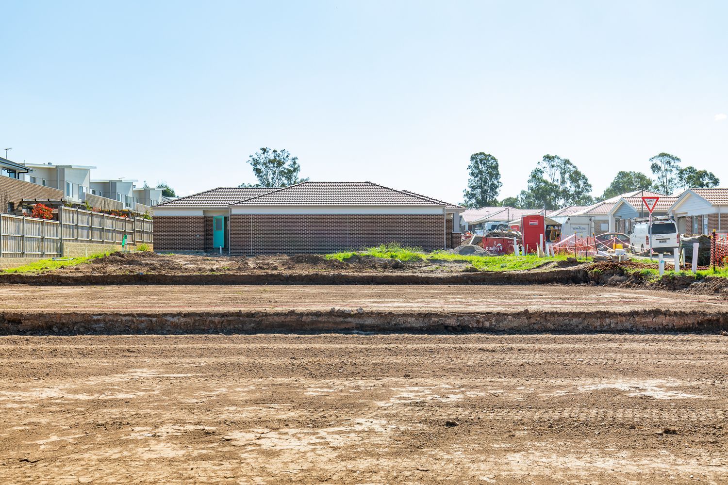 Cleared dirt lot with a brick house in the background at a new residential housing development under construction.