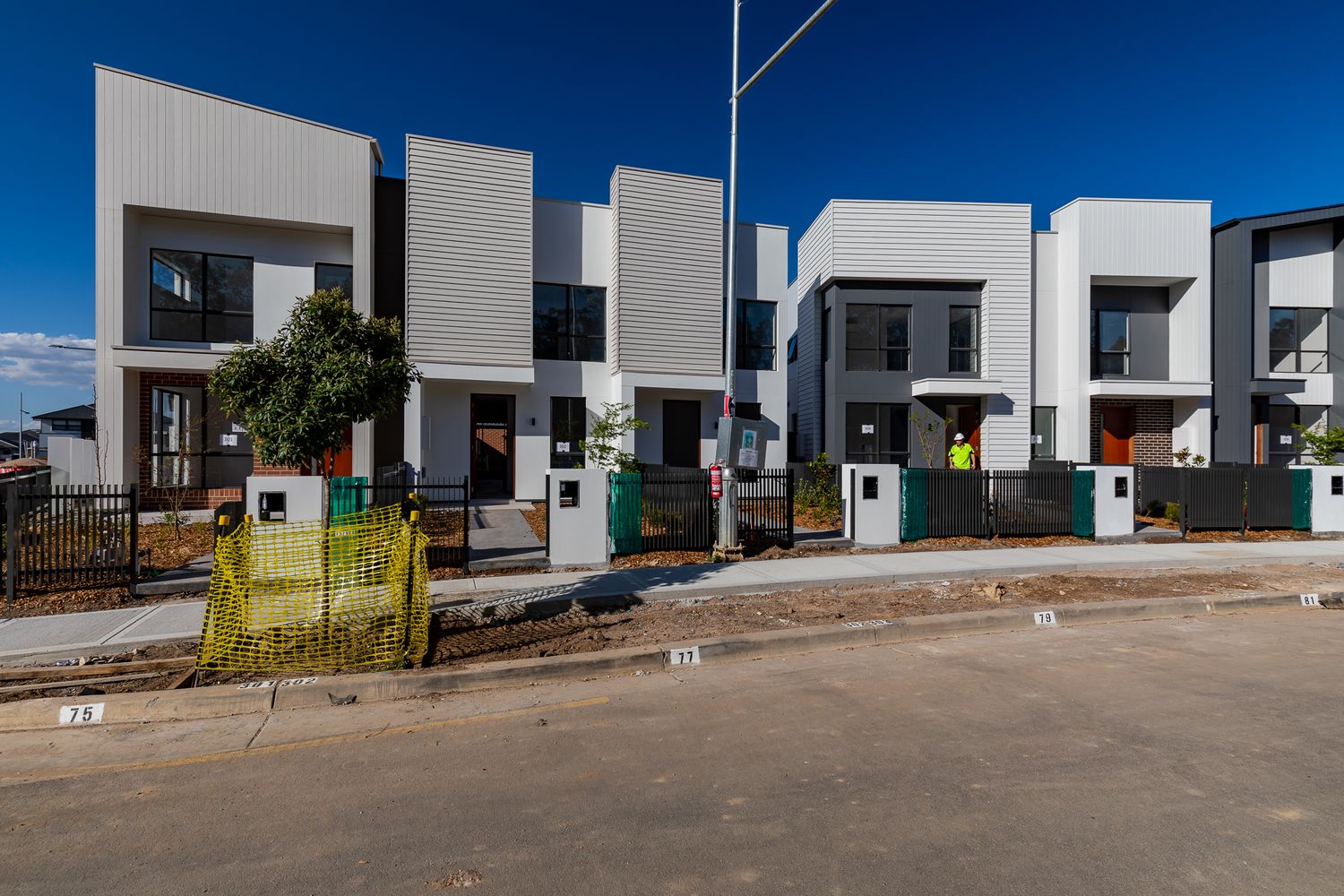 Row of new contemporary two-storey townhouses with white and grey facades and landscaped front gardens on a freshly paved street.