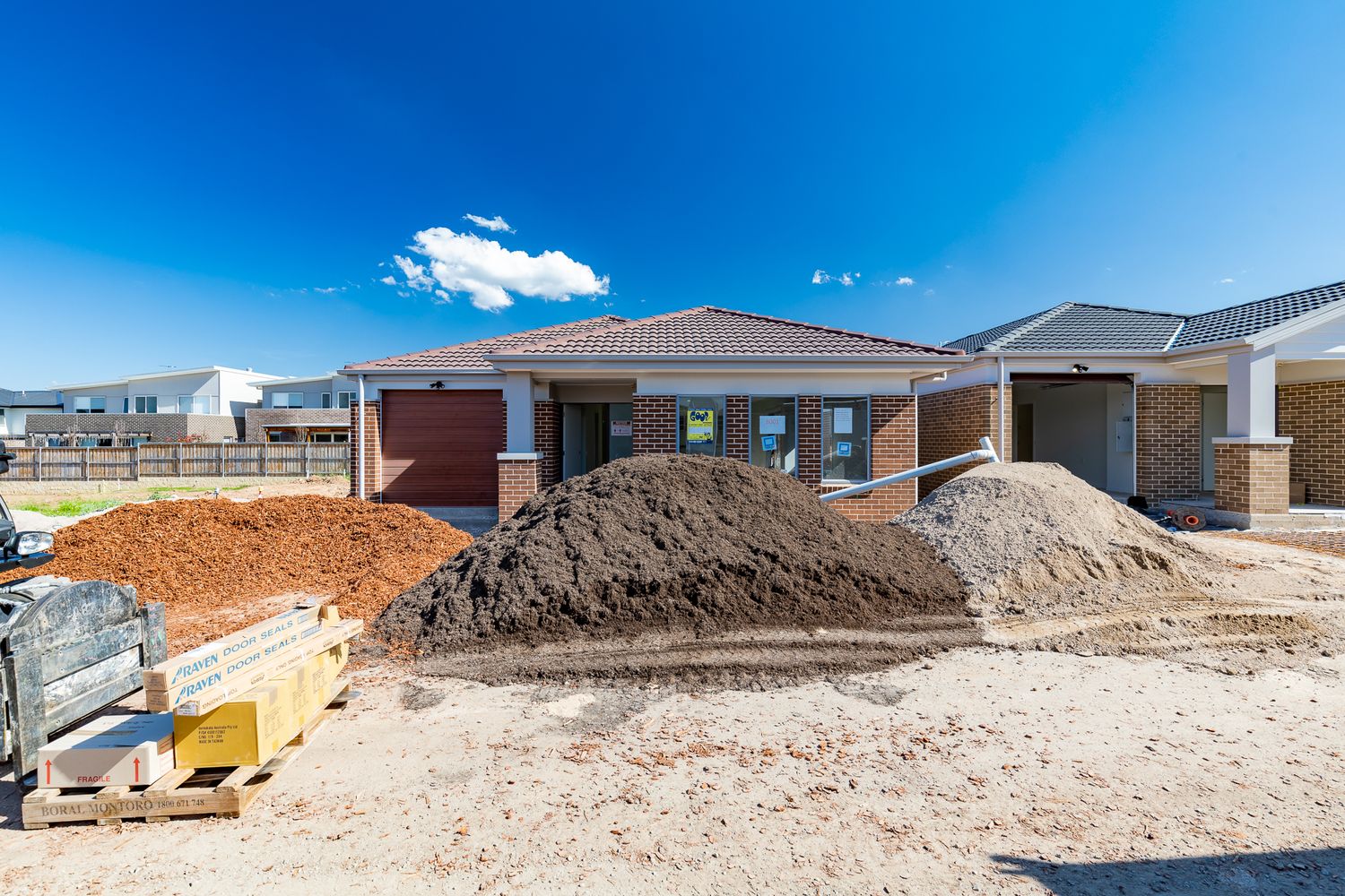 Brick house under construction with piles of soil and sand in the foreground and a clear blue sky above.
