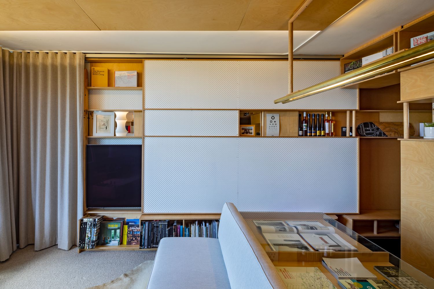 Multifunctional living room wall with sliding panels hiding the television and revealing wooden storage shelves.