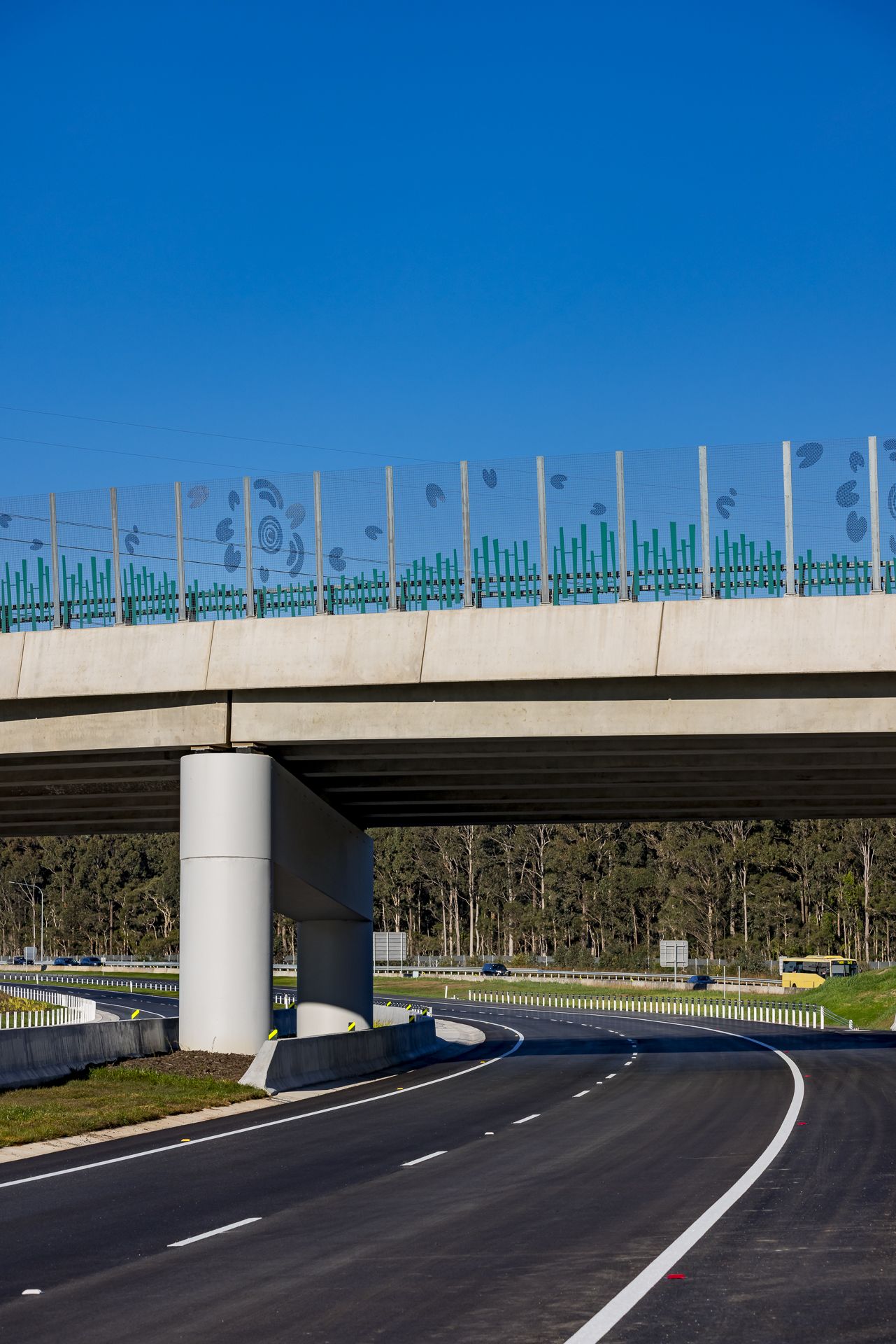 Concrete highway overpass with decorative blue patterned noise barrier panels above fresh asphalt and white lane markings.