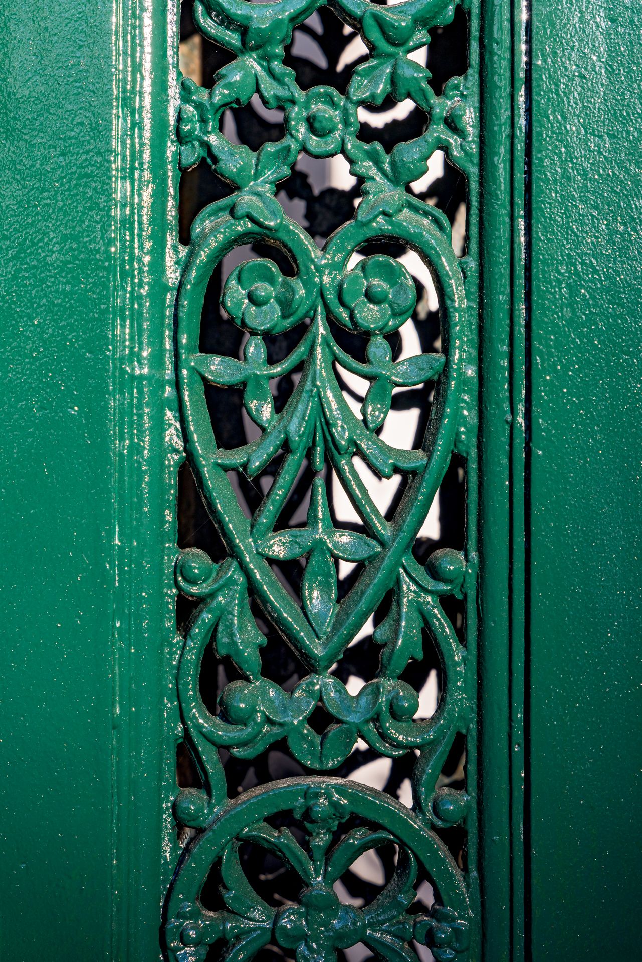 Close-up of a glossy green cast-iron panel with a heart-shaped floral lace pattern.