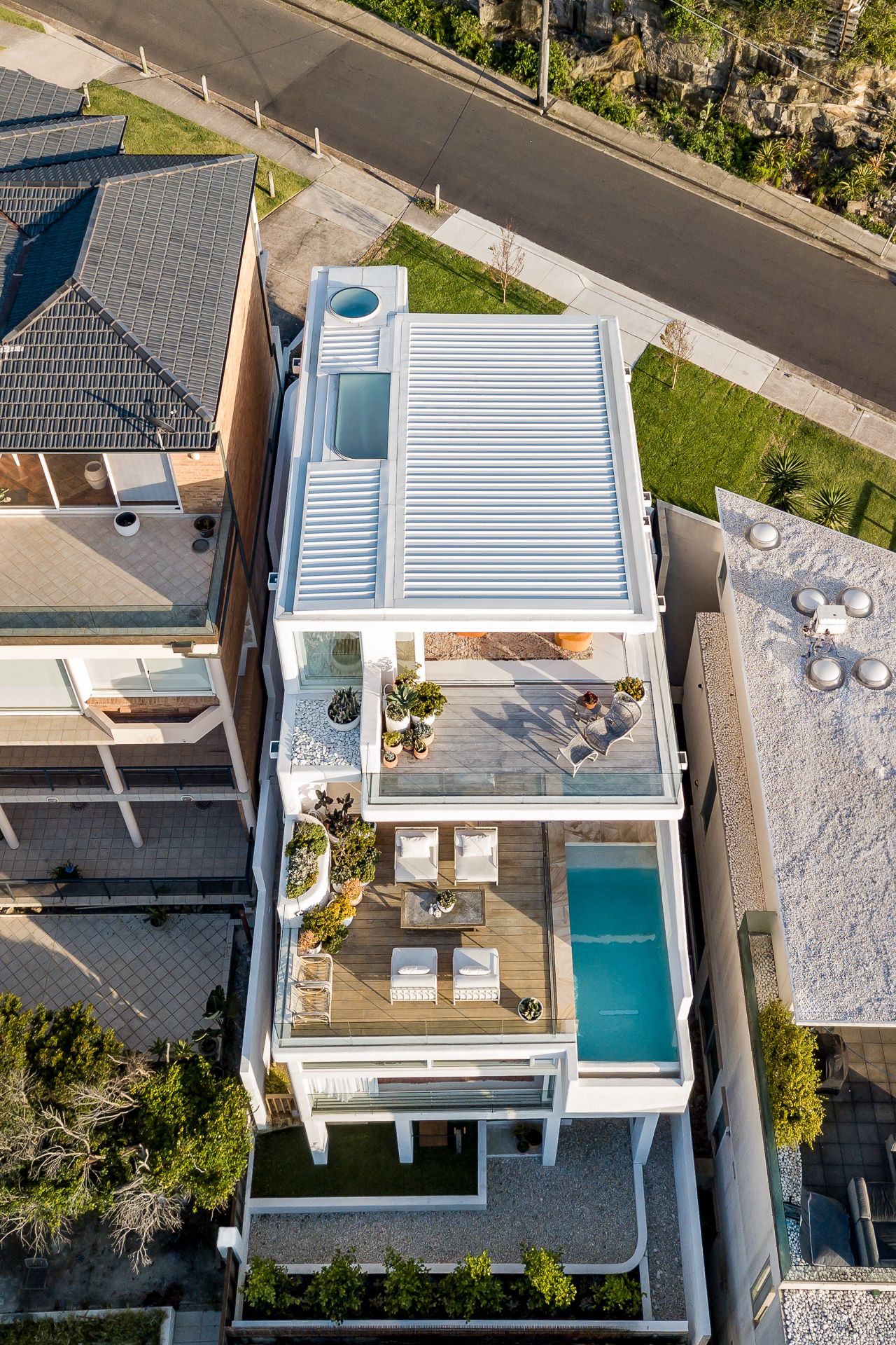 Aerial view of a contemporary white house with a corrugated roof, timber deck, and plunge pool.