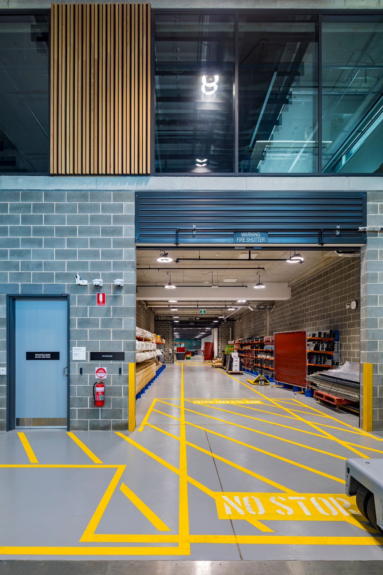 TAFE trade training storeroom entrance with yellow floor markings, concrete block walls, shelving and a timber slat feature above.