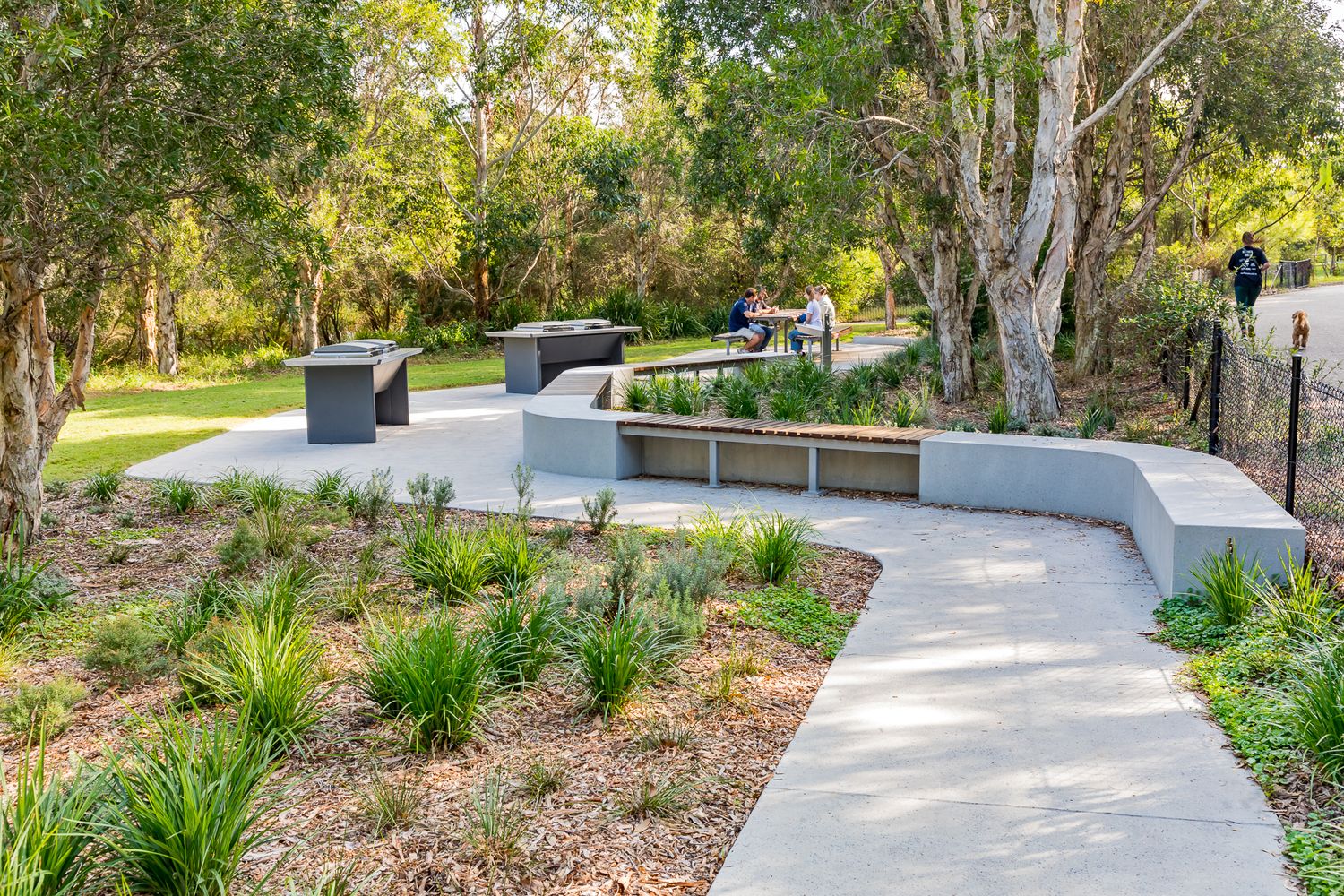 Rusty metal Sydney Park letters mounted on a sandstone wall above native grasses with a green lawn and trees in the background.
