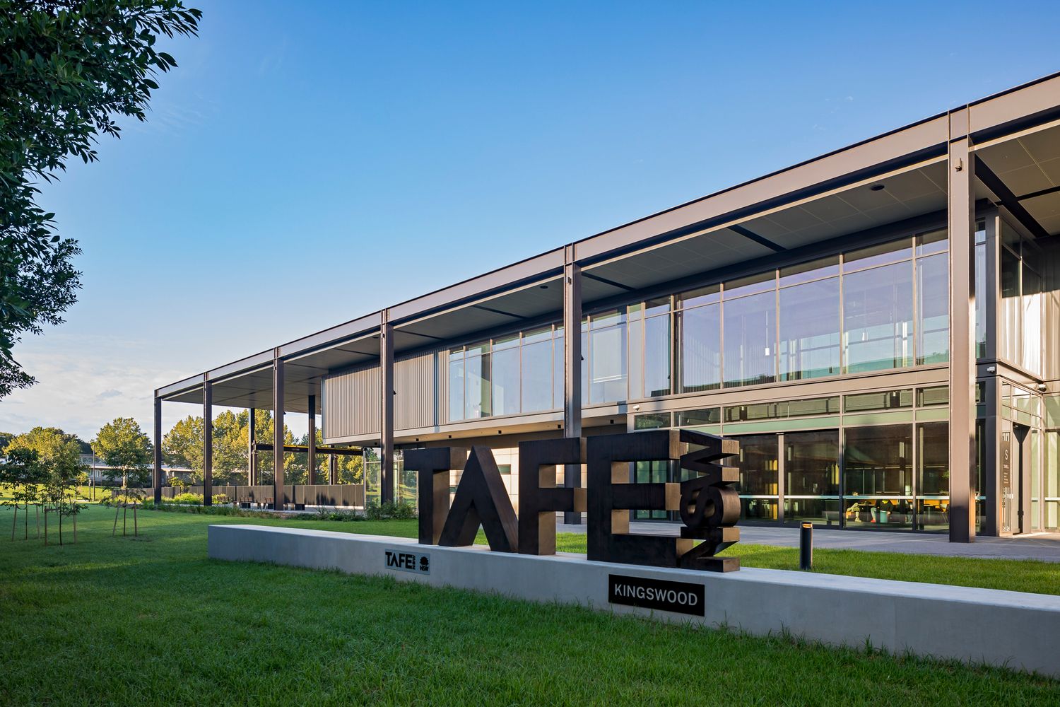 Large TAFE sign in front of a modern glass and steel education building with a landscaped lawn under a bright blue sky.
