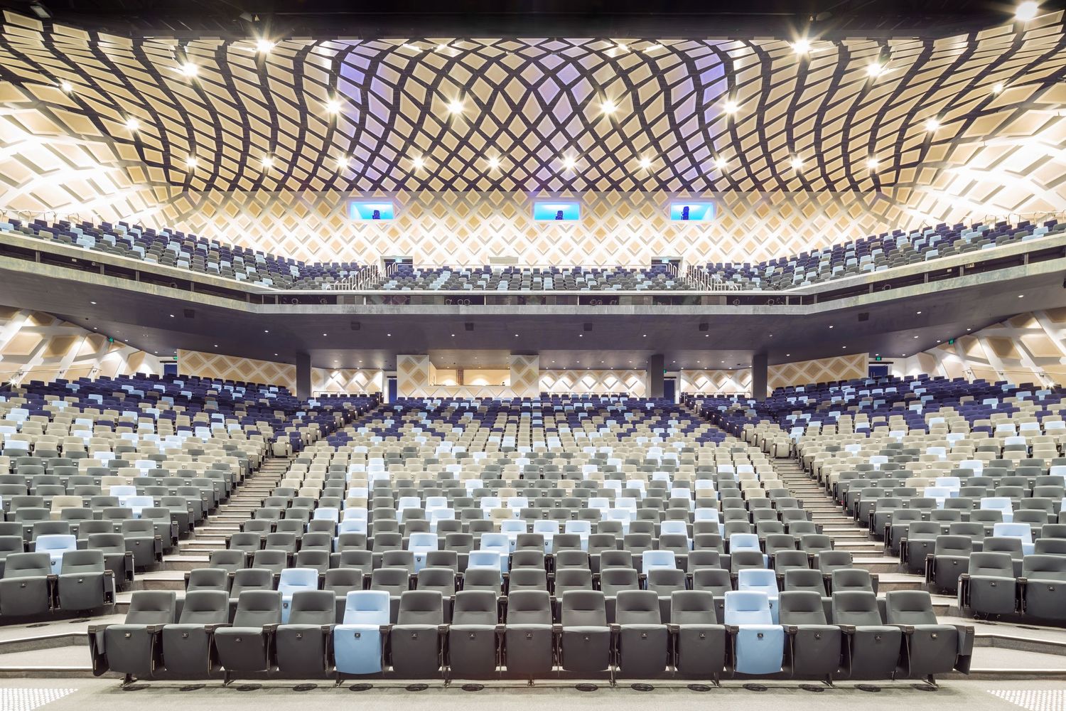 Spacious theatre with tiered grey seating, steps and an ornate patterned timber ceiling above the upper balcony.