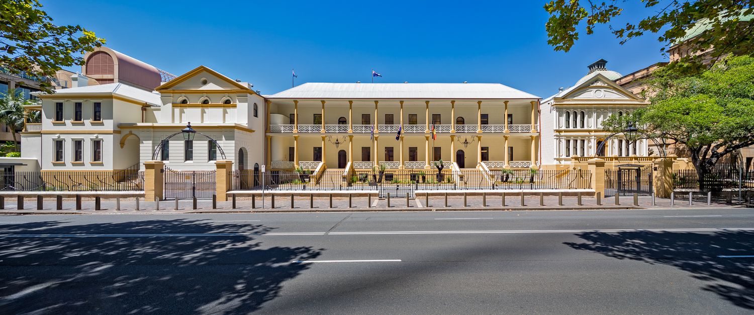 Historic three-storey colonial government building with columned verandas, viewed across a street under a clear blue sky.