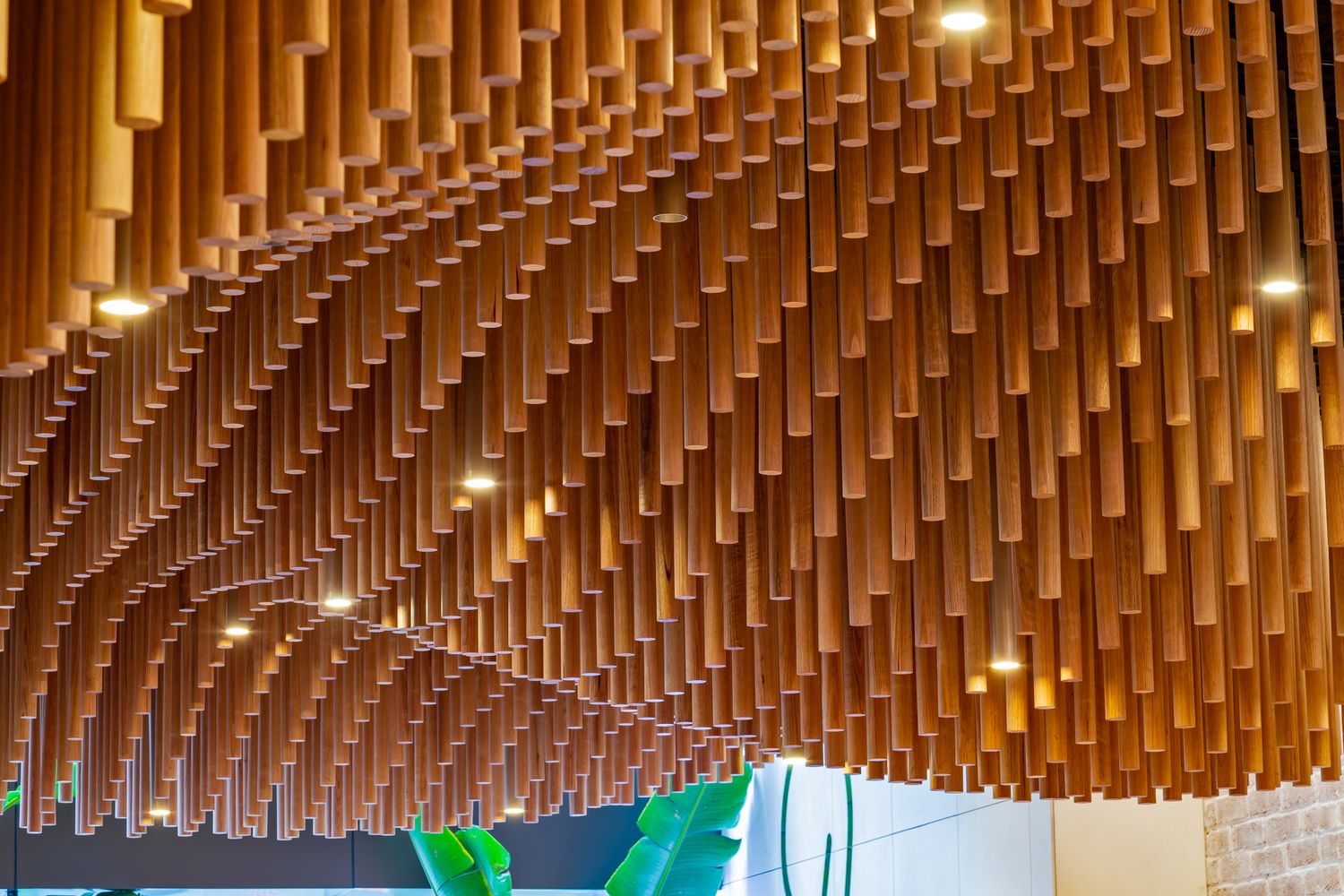 Close view of hundreds of vertical timber tubes forming an undulating ceiling sculpture with small recessed lights in a cafe.