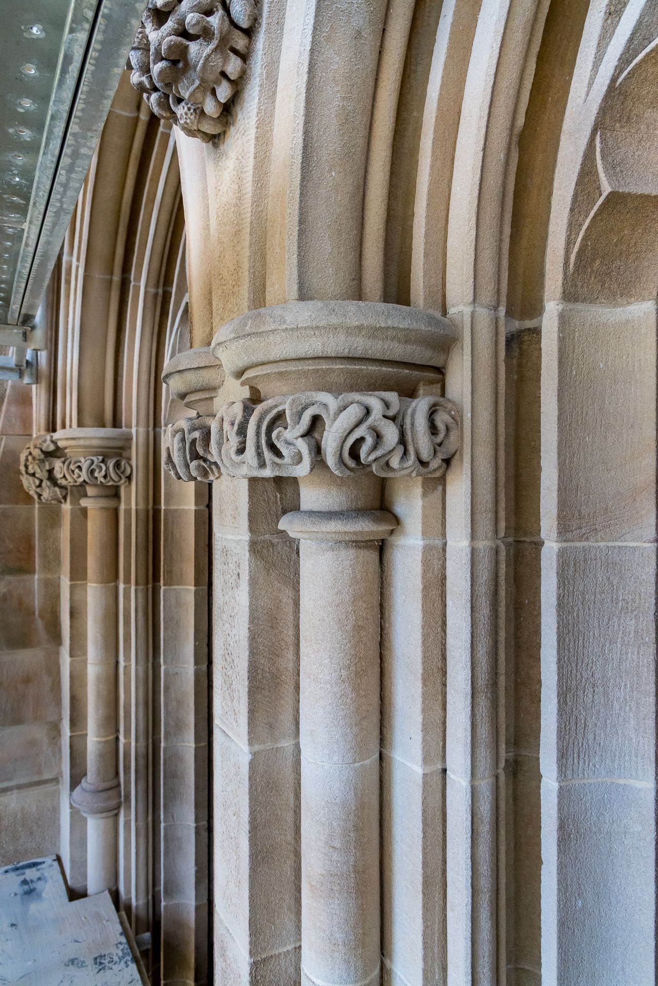 Row of sandstone pillars with carved scrolled capitals along a Gothic arcade in a historic stone building.