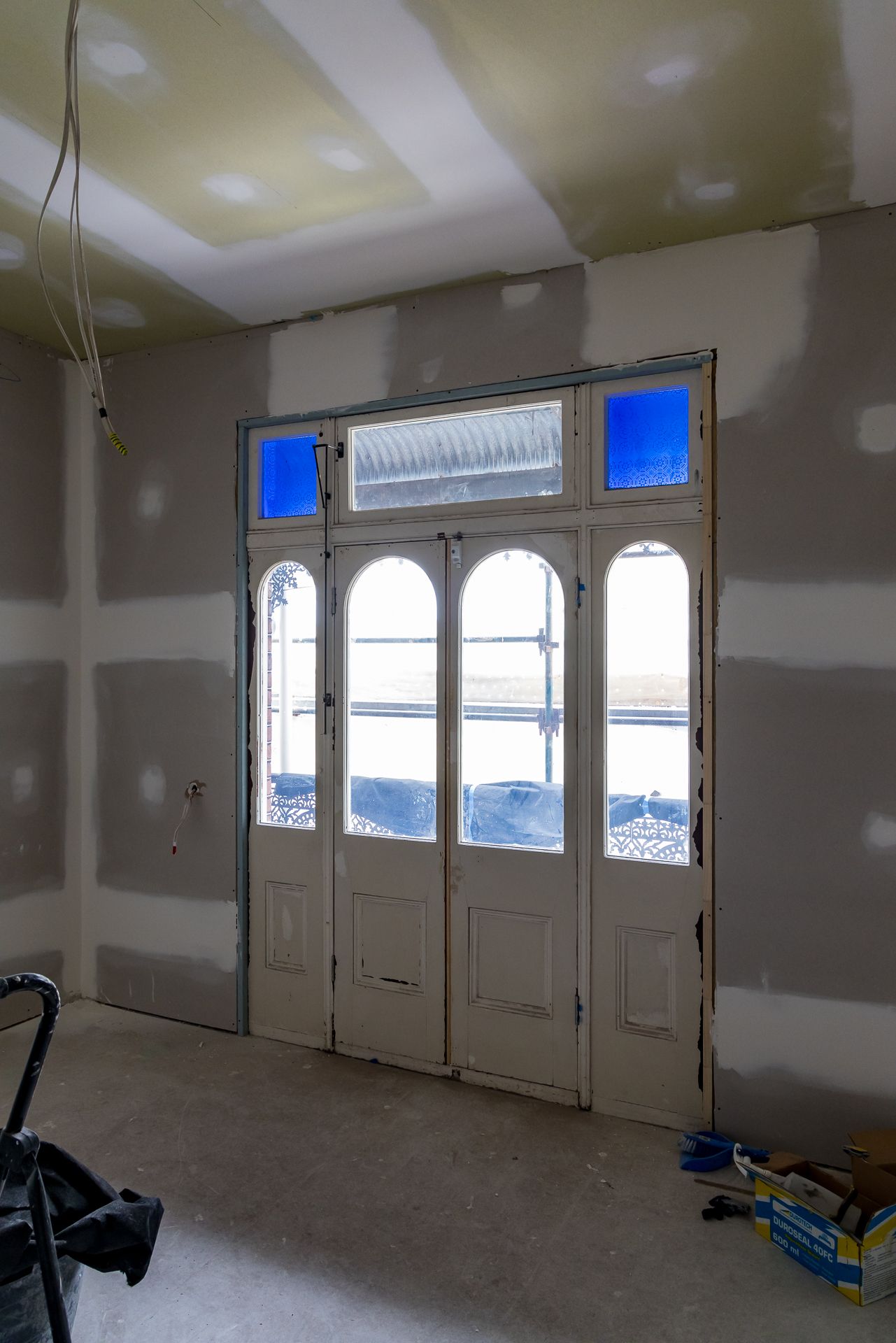 Unfinished entry hallway with plasterboard walls and a heritage timber door with arched glass panes and blue glass highlights.