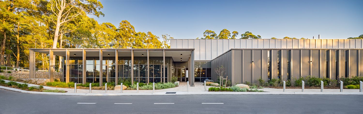 Modern single-storey research building with a glass-fronted entrance and metal cladding set among tall eucalyptus trees under a blue sky.