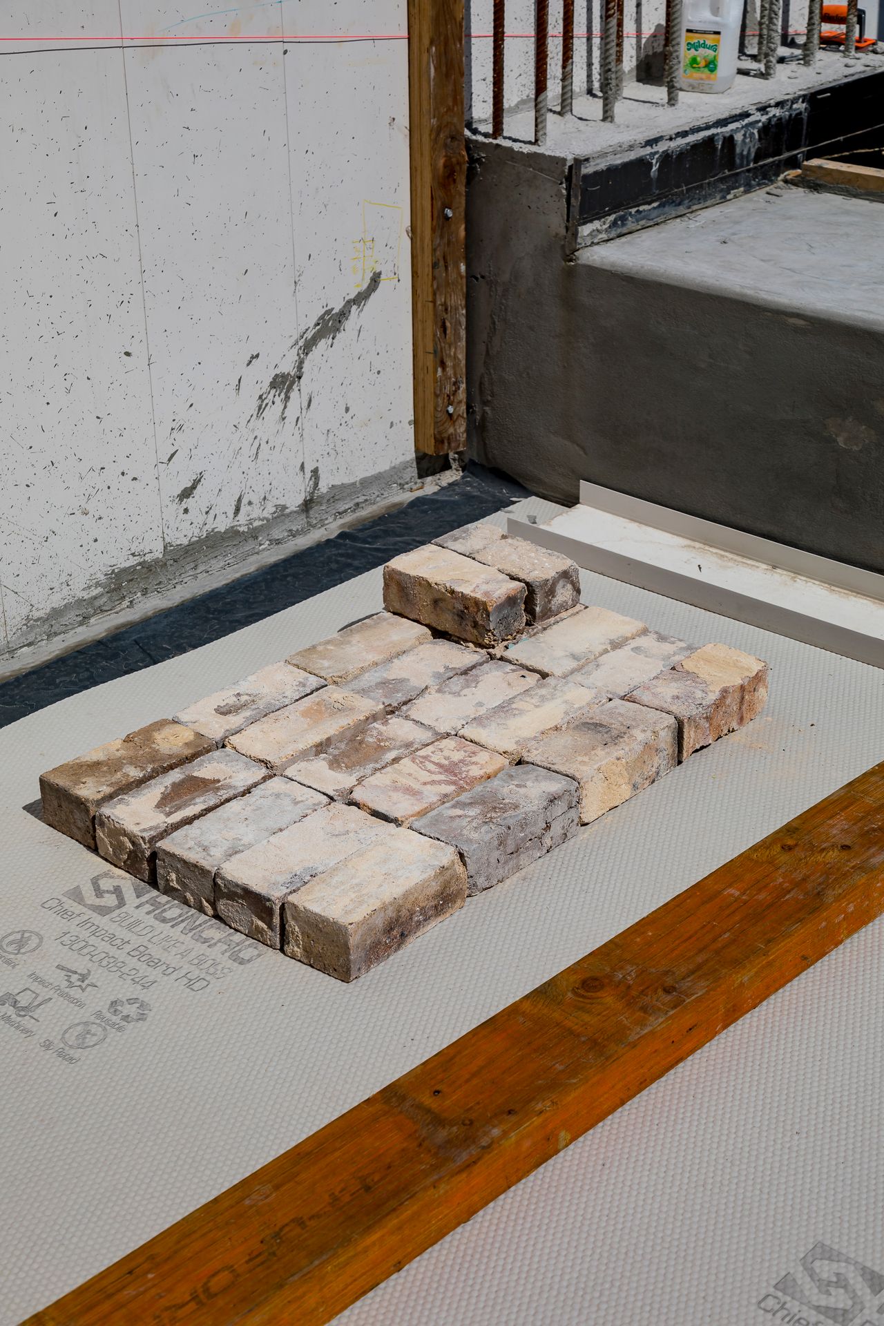 Reclaimed bricks stacked in a neat pattern on protective floor sheeting beside a timber beam on a renovation site.