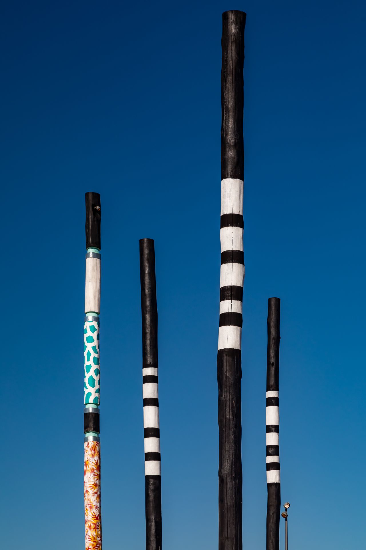 Four tall black poles with white stripes and colourful patterned sections rise against a deep blue sky.