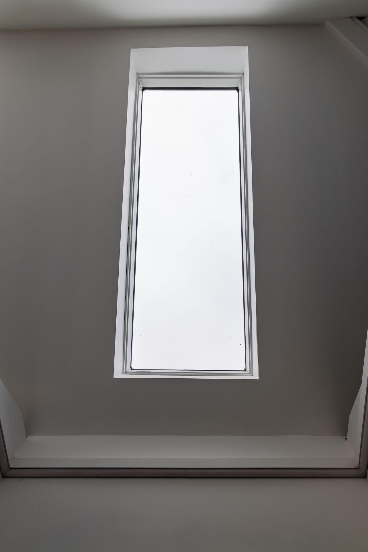 Tall narrow skylight viewed from below, set into a plain white ceiling shaft in a renovated home.
