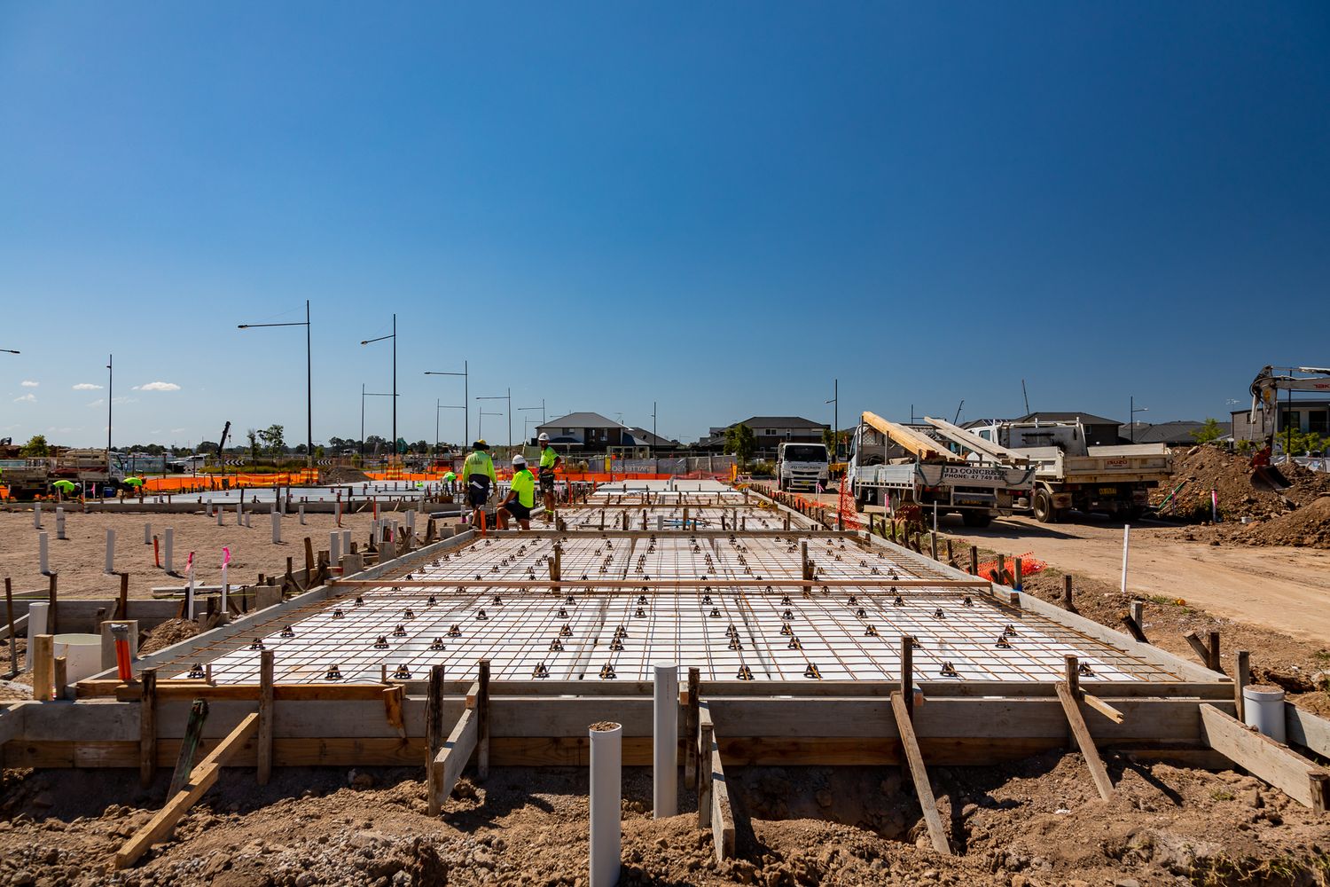 Wide view of a reinforced concrete slab foundation with timber formwork and steel mesh at a residential development site.