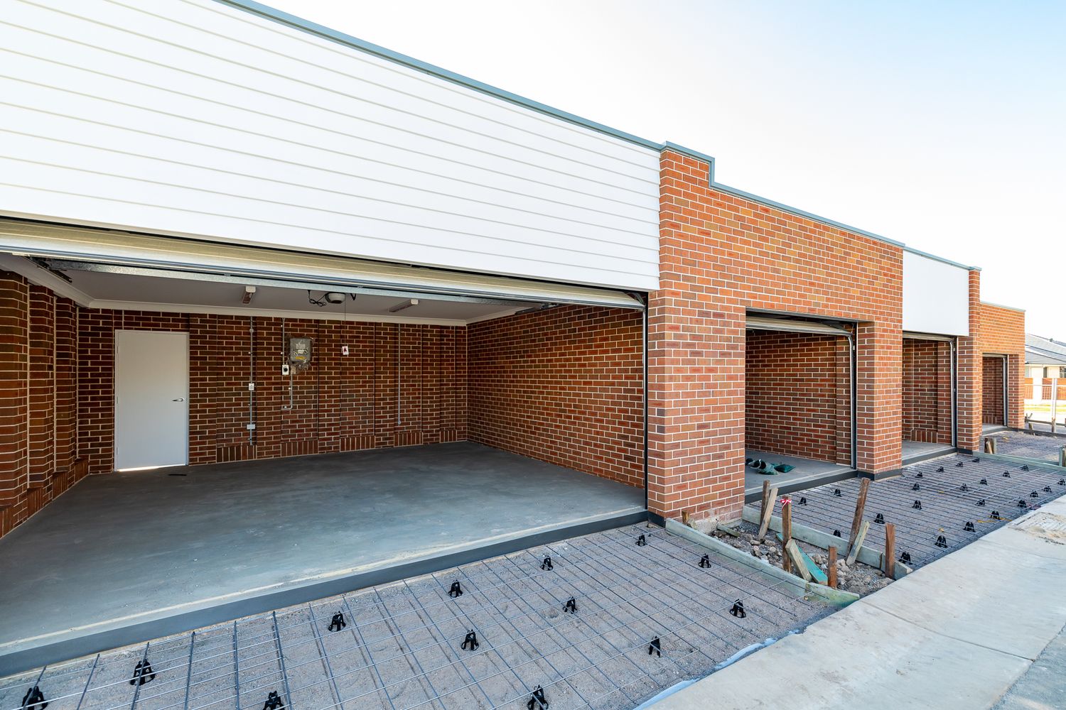 Single-storey brick townhouses with open garages, white cladding and a concrete driveway in a new residential development.