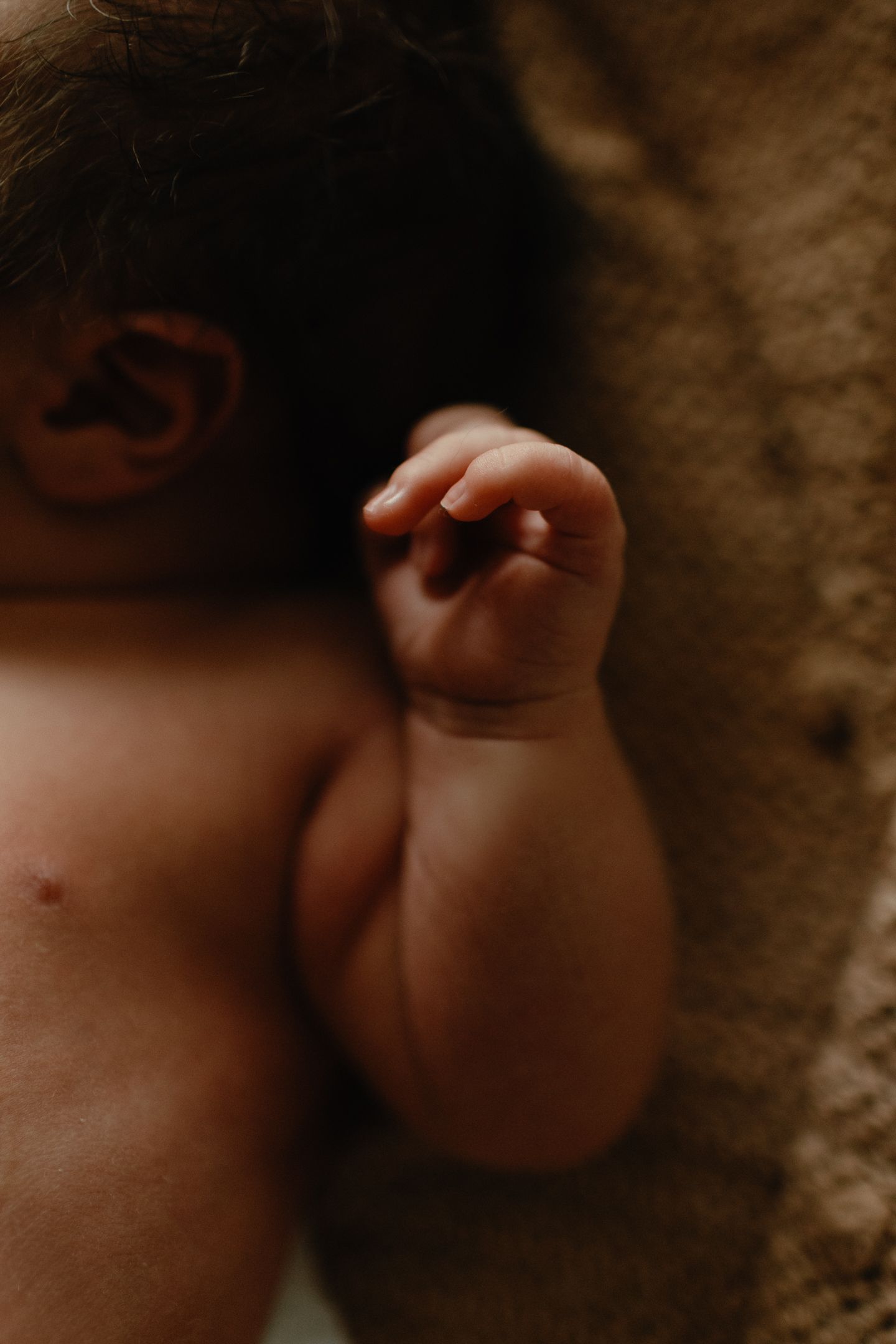 Close-up of a sleeping newborn's tiny curled hand and arm resting on a soft beige blanket.