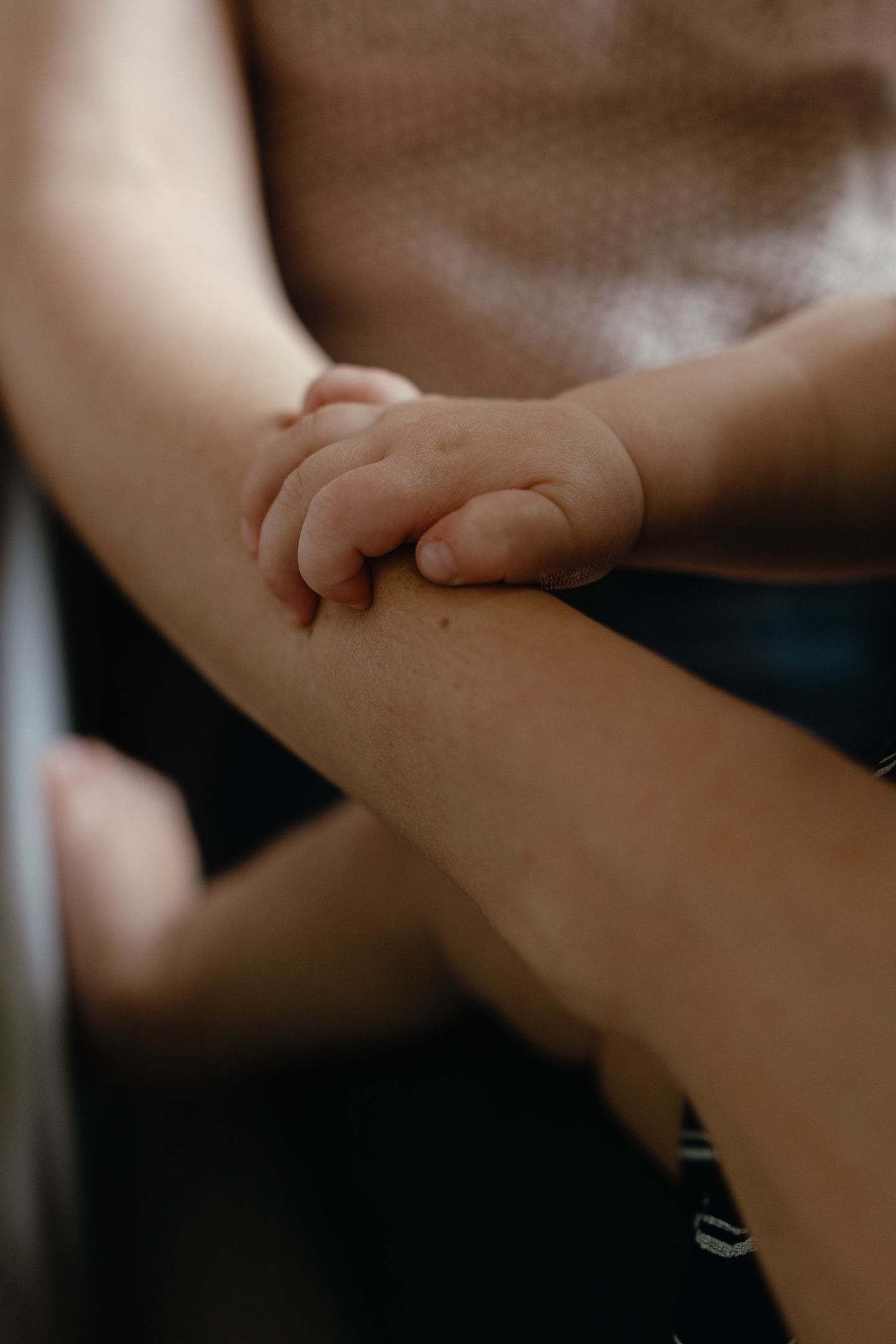 Close-up of a tiny baby hand resting on a mother's forearm, capturing a tender bond between parent and child.