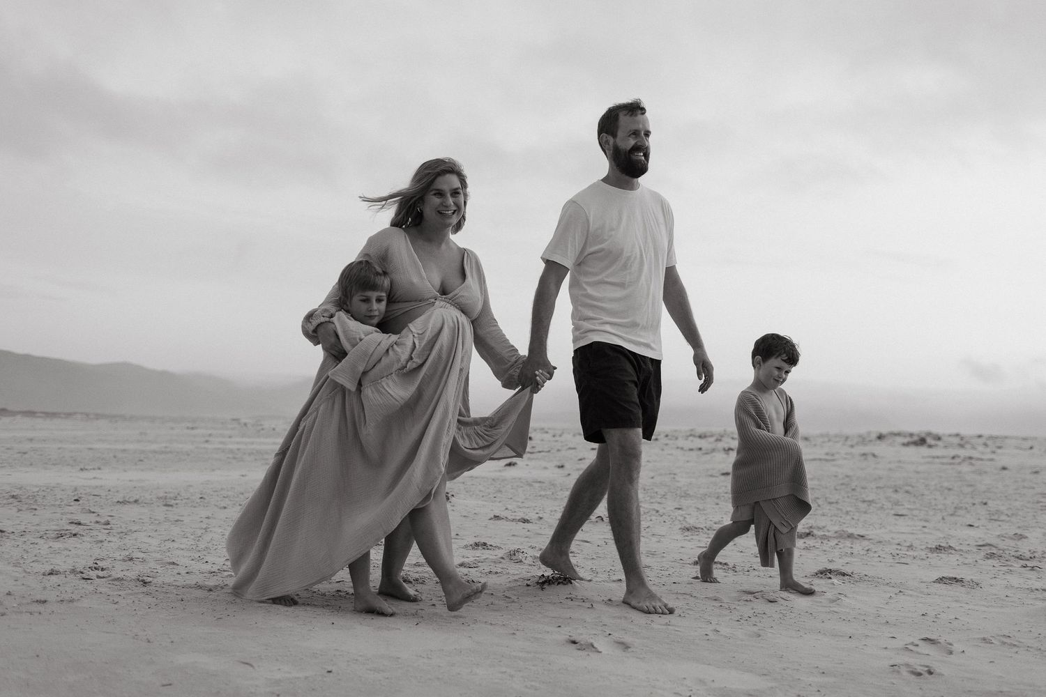 Black and white photo of parents and two children walking hand in hand along a sandy beach.