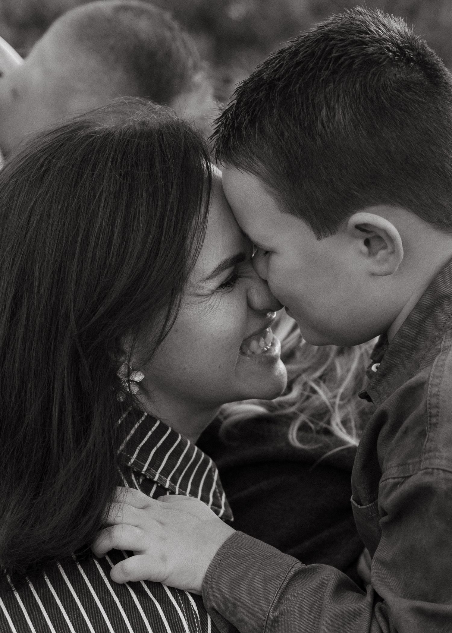 A black and white portrait of a smiling mother touching foreheads with her young son in a tender, affectionate family moment.