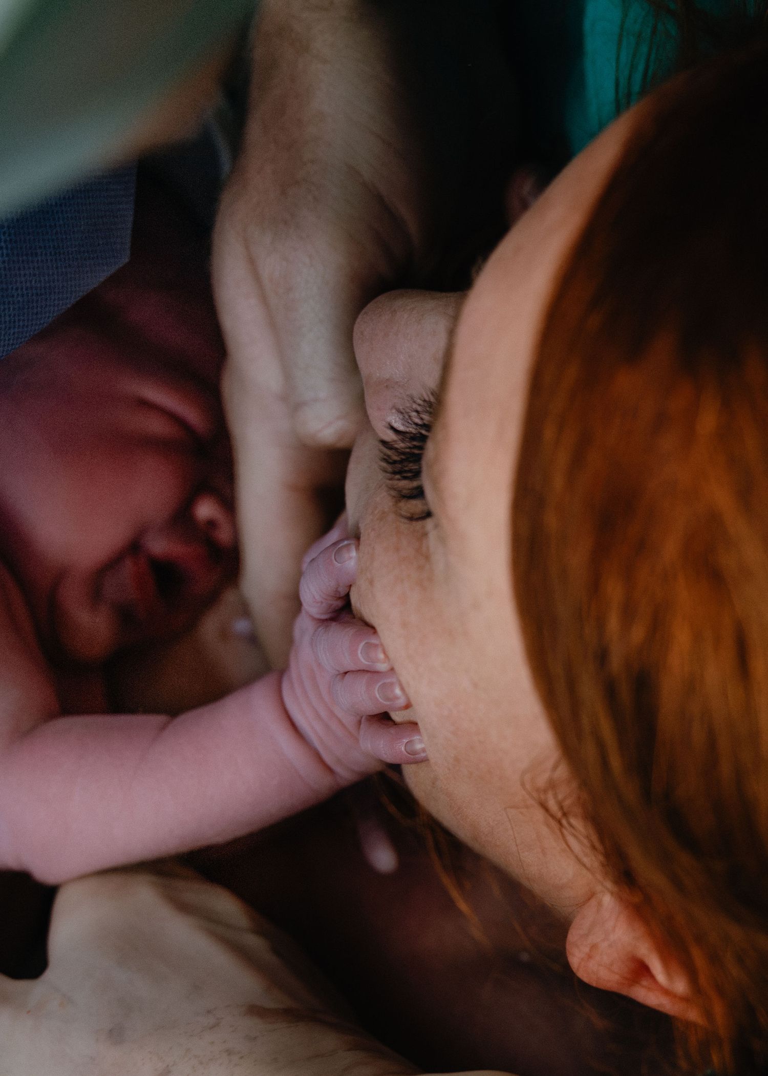 A newborn baby's tiny hand rests on a red-haired mother's cheek as she closes her eyes in a tender moment after birth.