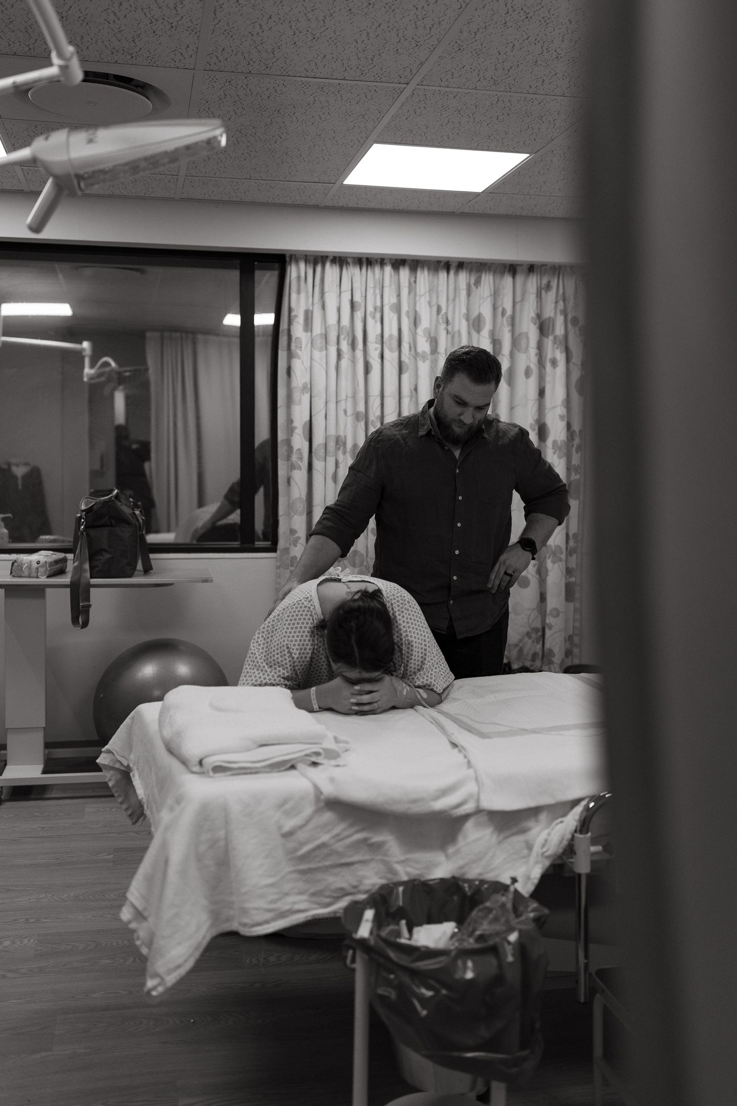 Black and white photo of a man comforting a woman leaning over a hospital bed during labor in a delivery room.