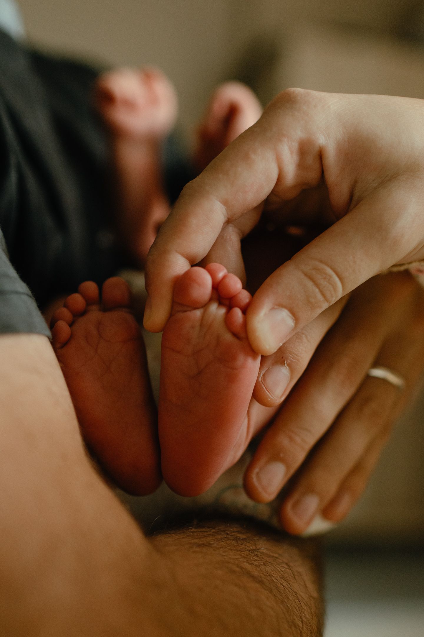 Close-up of a parent's hands gently holding the tiny bare feet of a newborn baby in a warm, softly lit indoor setting.