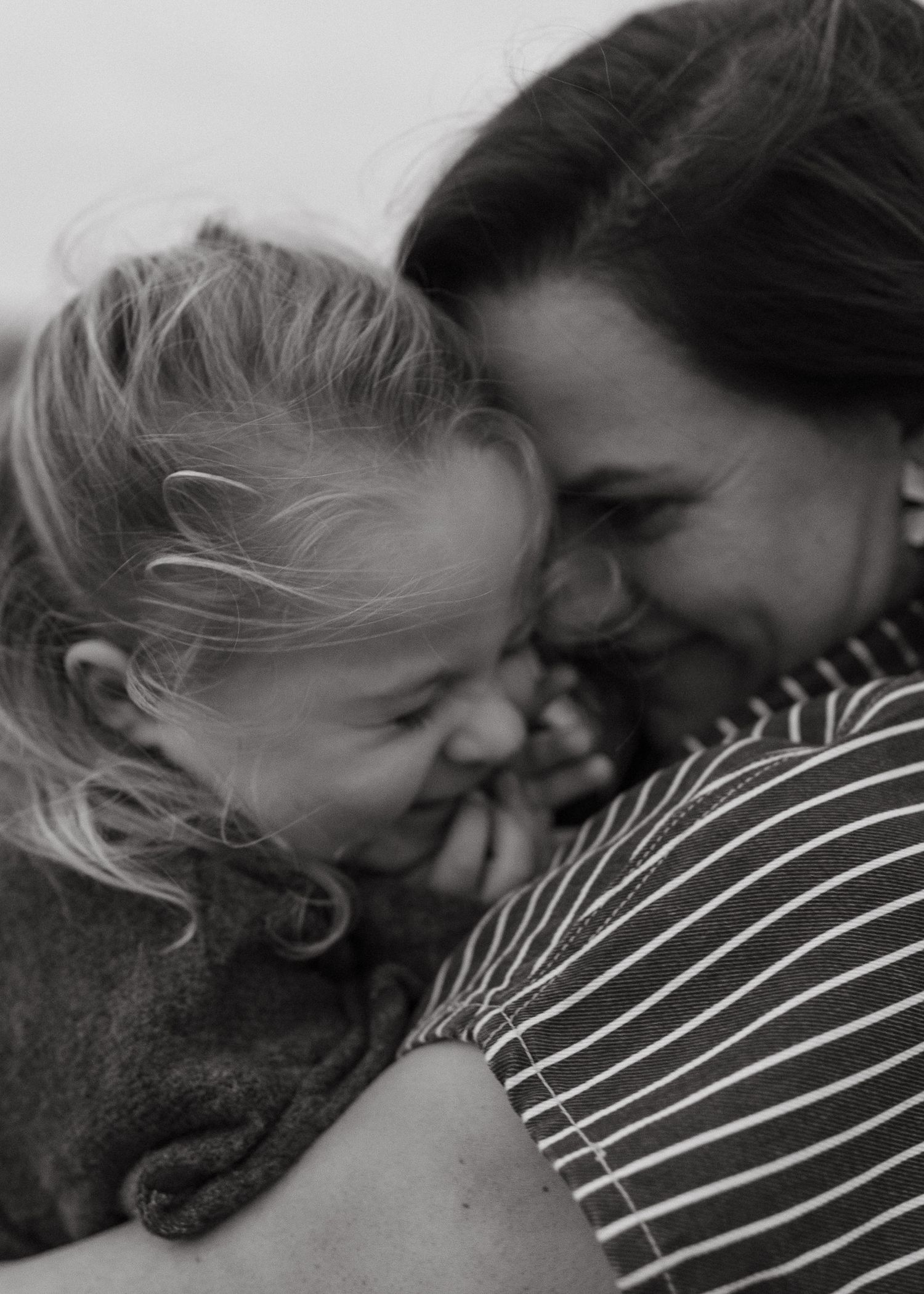 Black and white close-up of a laughing little girl hugging her smiling mother in a striped shirt.