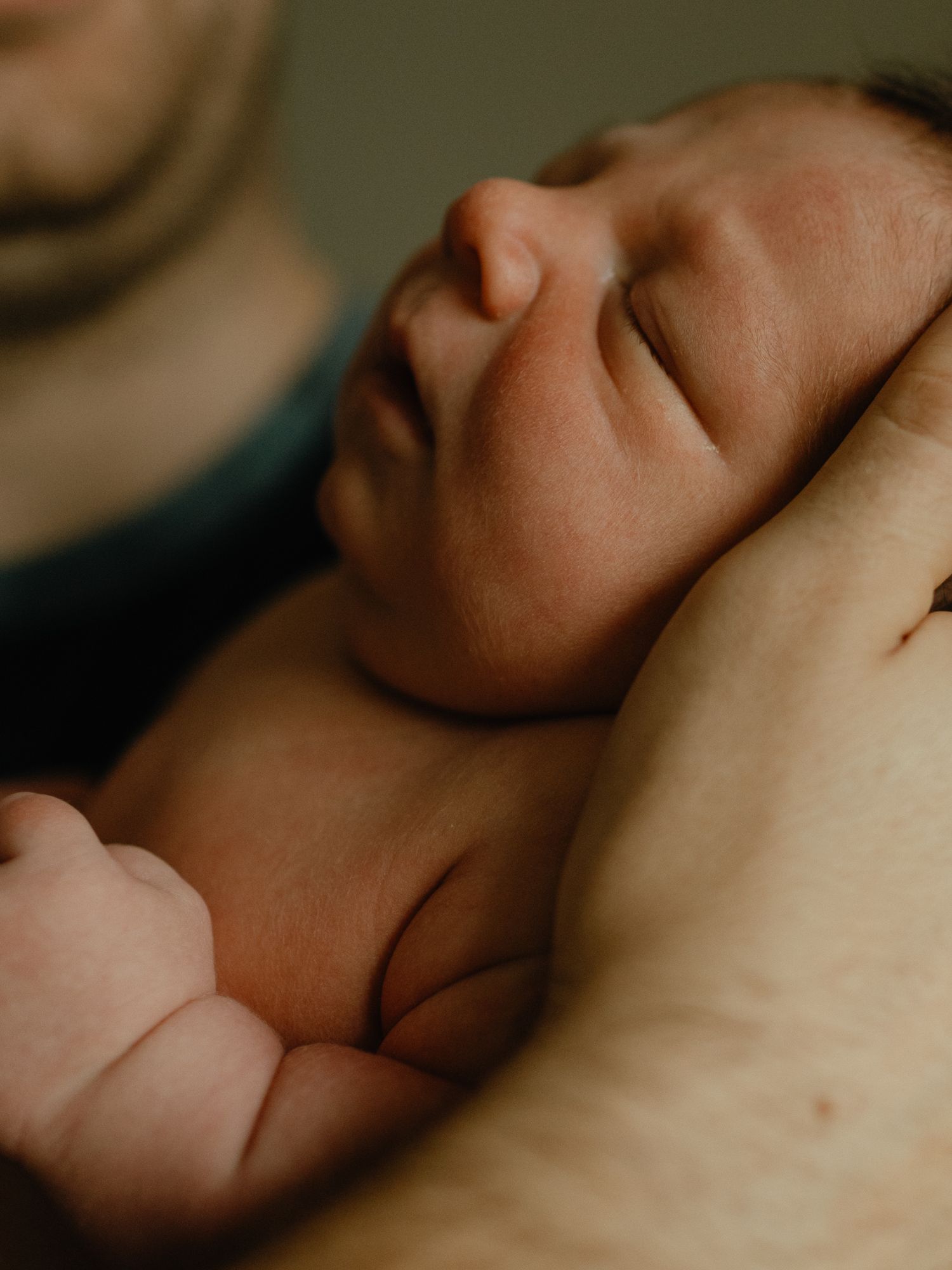 Sleeping newborn baby rests peacefully in a father's cupped hands, face softly lit with a cozy glow.