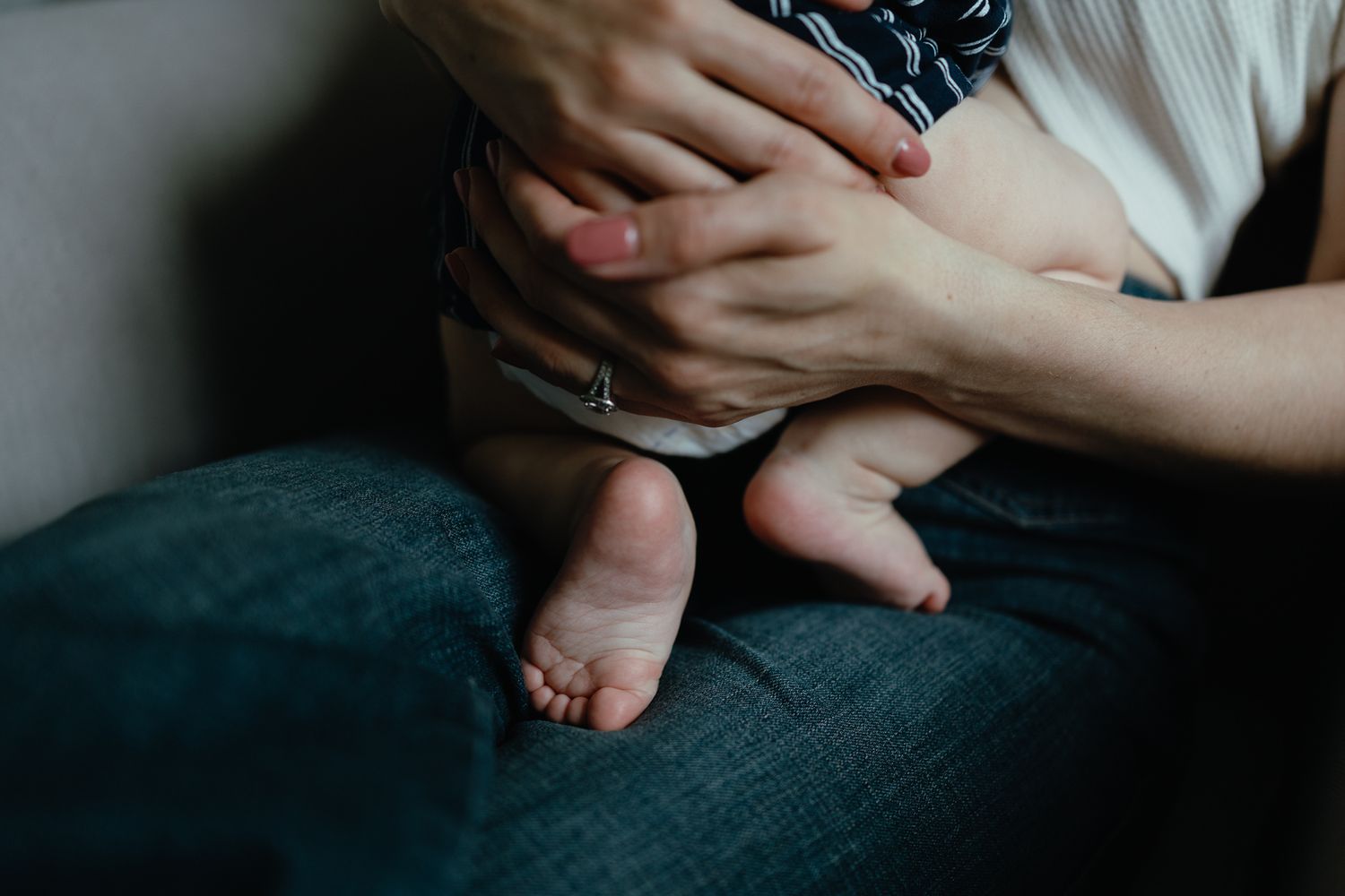 A close-up of a baby's bare feet as a mother holds the infant in her lap, wearing jeans and a ring.