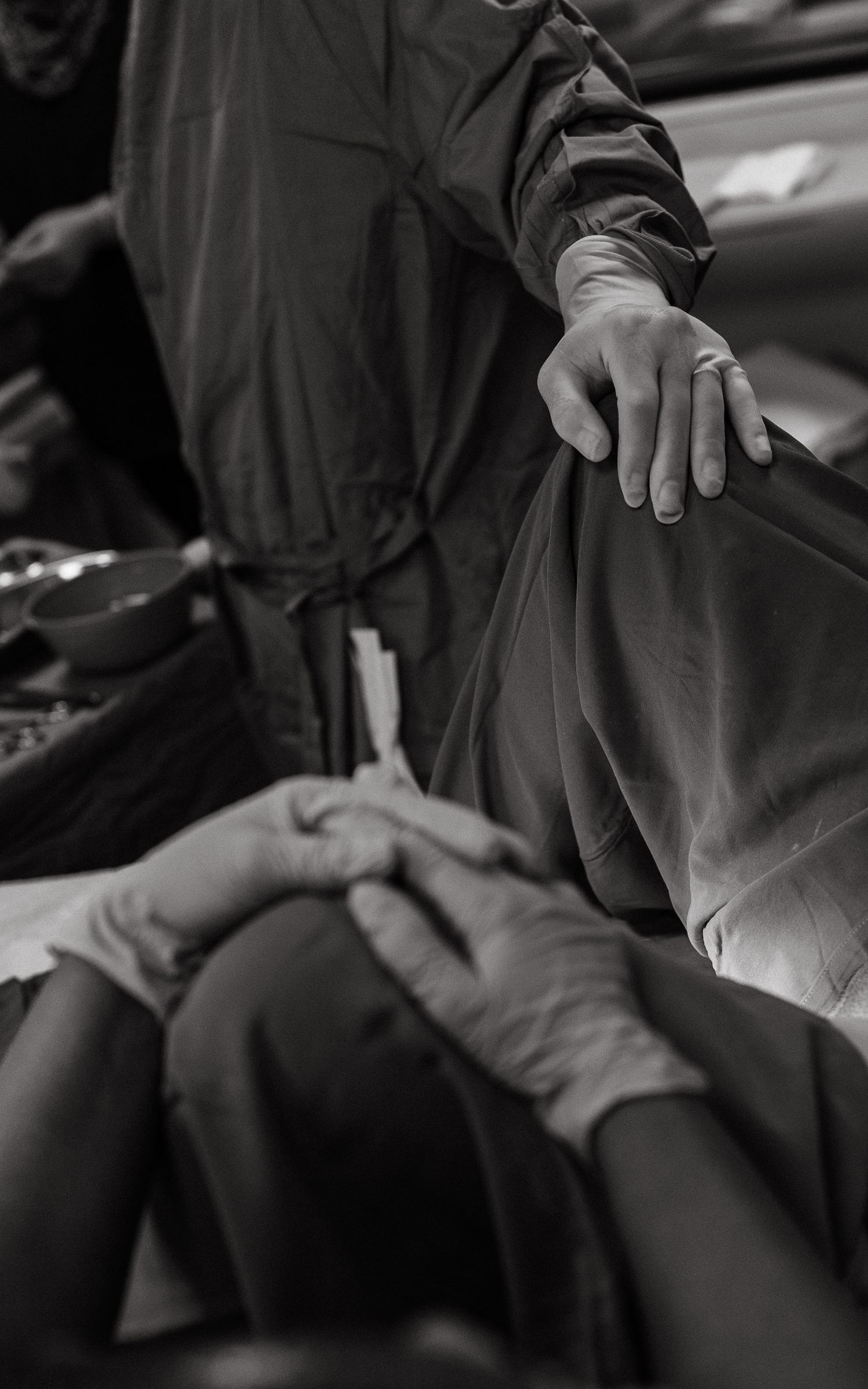 Black and white birth photograph showing a gloved medical team in surgical gowns attending a mother during delivery in a hospital room.
