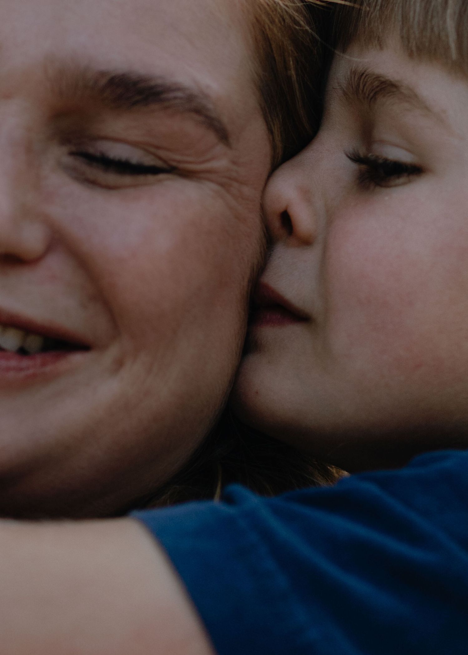 Close-up of a smiling mother with eyes closed as her young son affectionately kisses her cheek.