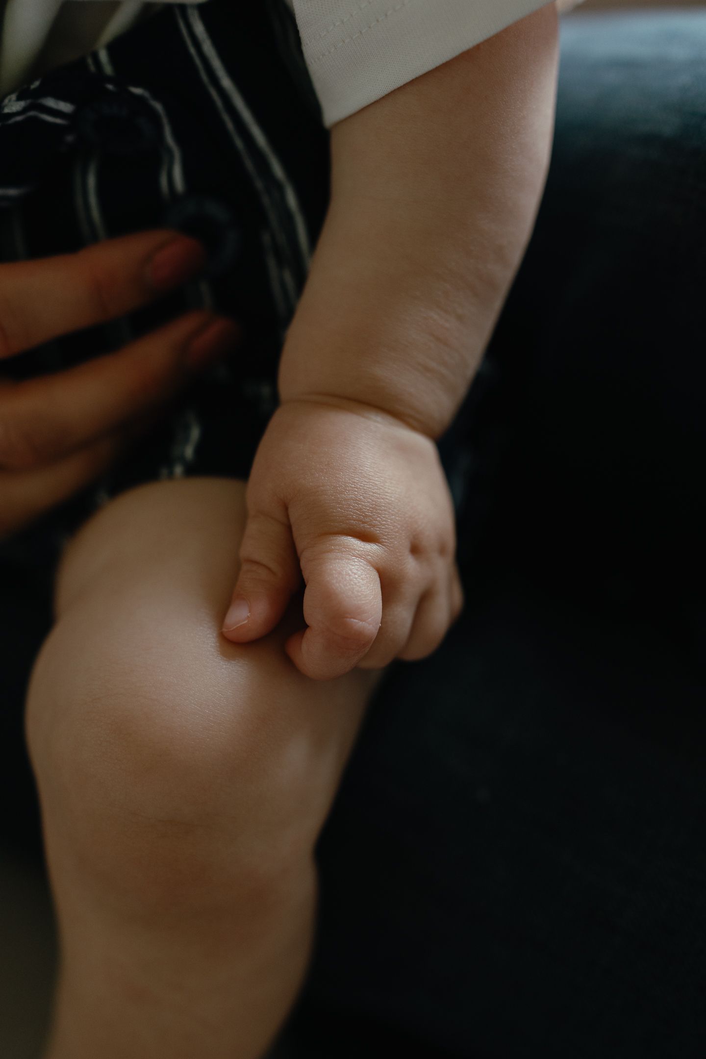 Close-up of a baby's chubby hand resting on his knee beside a mother's hand with red nail polish.