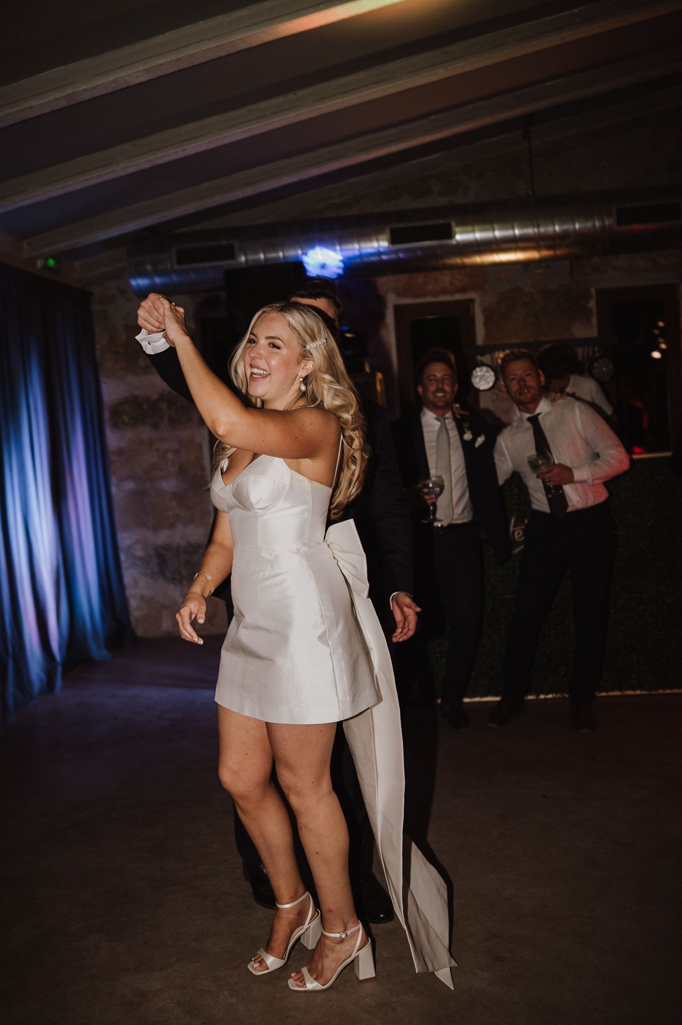 Joyful bride in short white mini dress dances energetically on the wedding reception dance floor.
