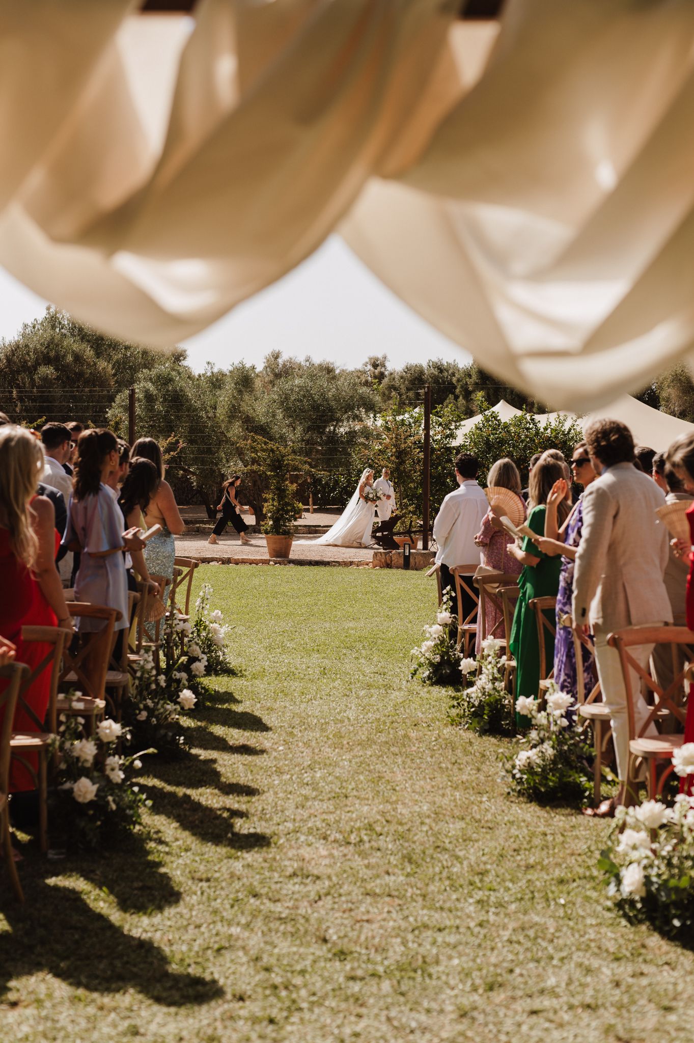 Elegant outdoor wedding ceremony aisle lined with floral arrangements and seated guests.