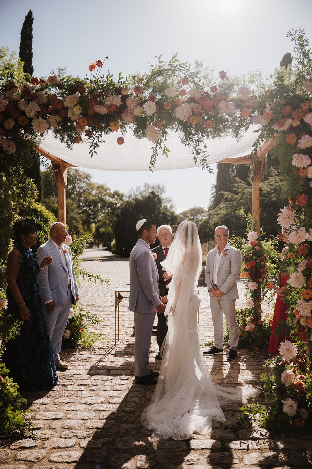 Couple exchanges vows under floral arch at outdoor wedding ceremony.