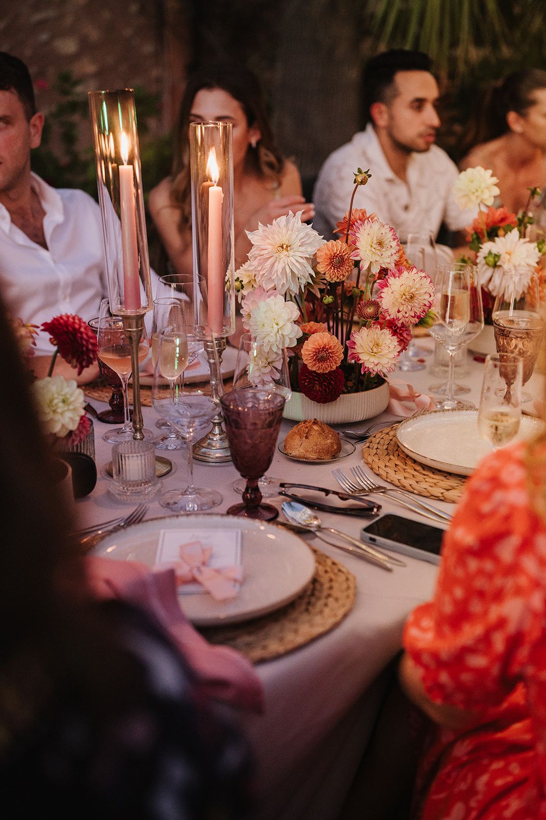 Elegant candlelit wedding dinner table with pink dahlias, tapered candles, and woven chargers.