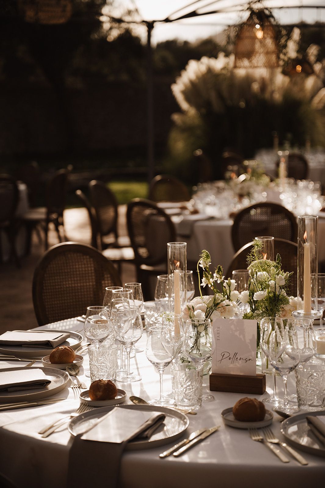 Elegant outdoor wedding reception table set with crystal glasses, candles, and floral centerpieces.